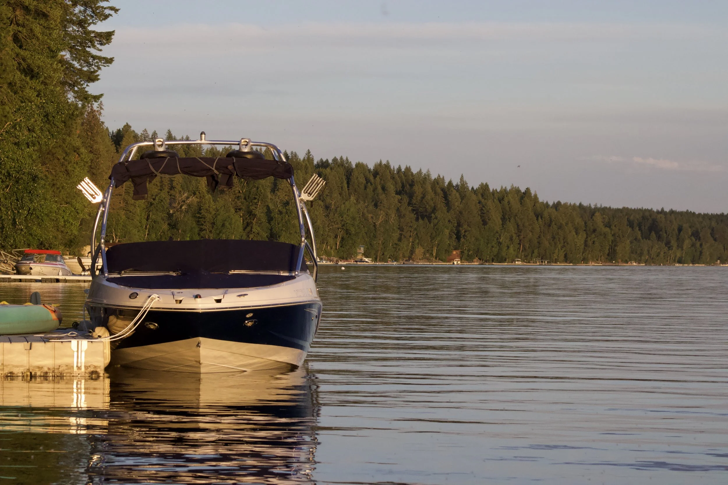 A boat docked at a pier on a calm lake, surrounded by trees during sunset.