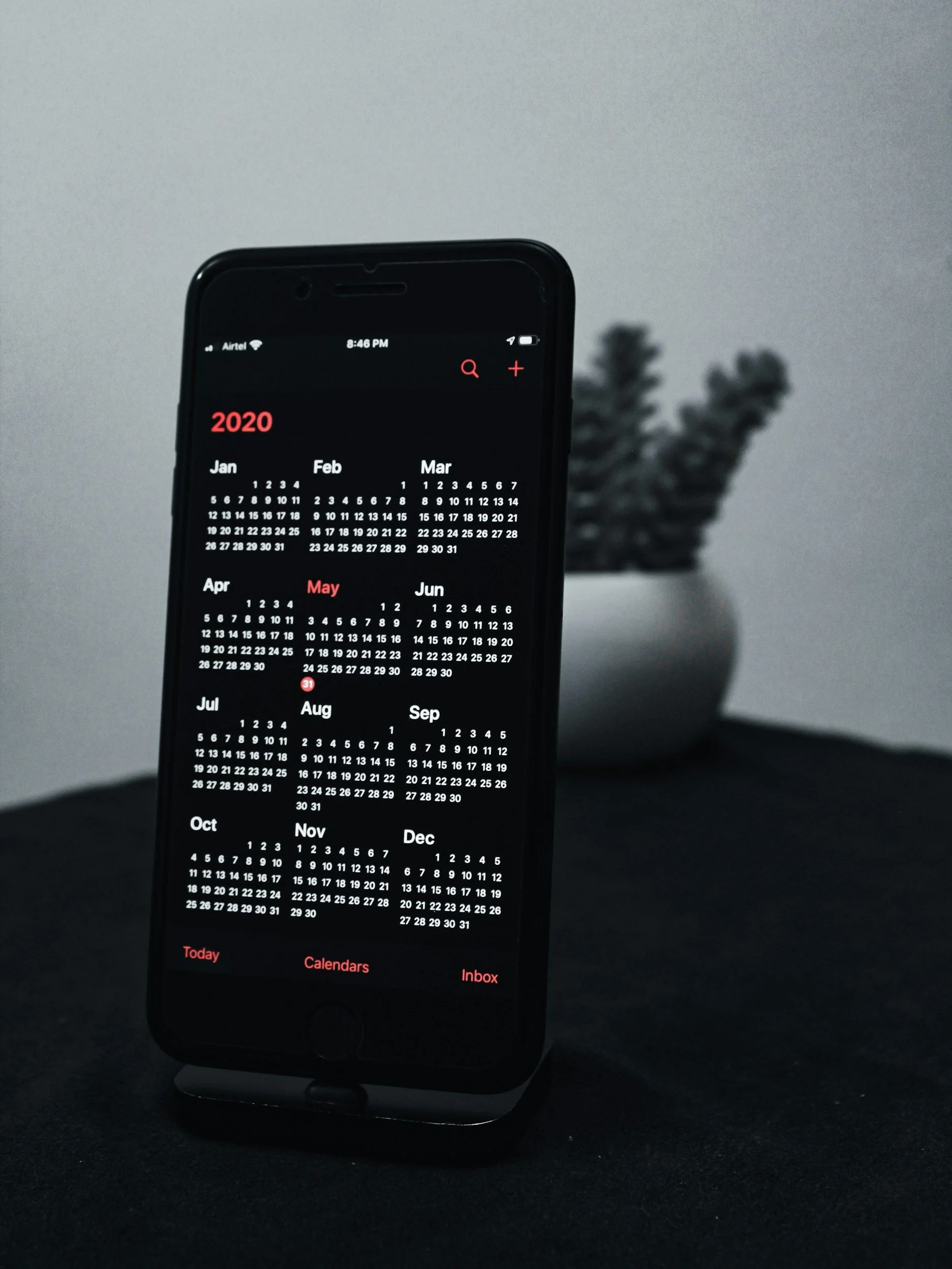 Smartphone displaying a 2020 calendar app on a black surface, with a potted plant in the background.
