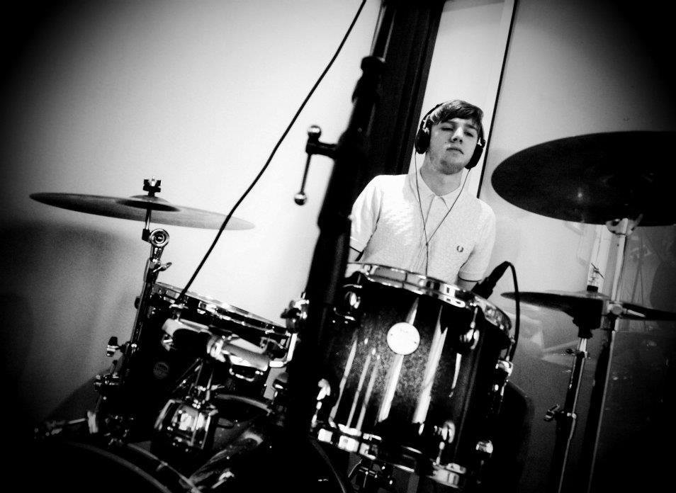 Young man with headphones sitting behind a drum set in a recording studio.