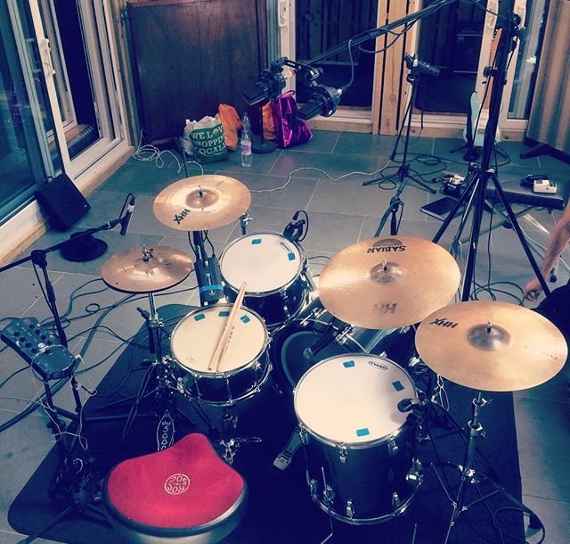 A drum set on a gray tiled floor with various electronic and recording equipment around it, in a recording studio or music room.