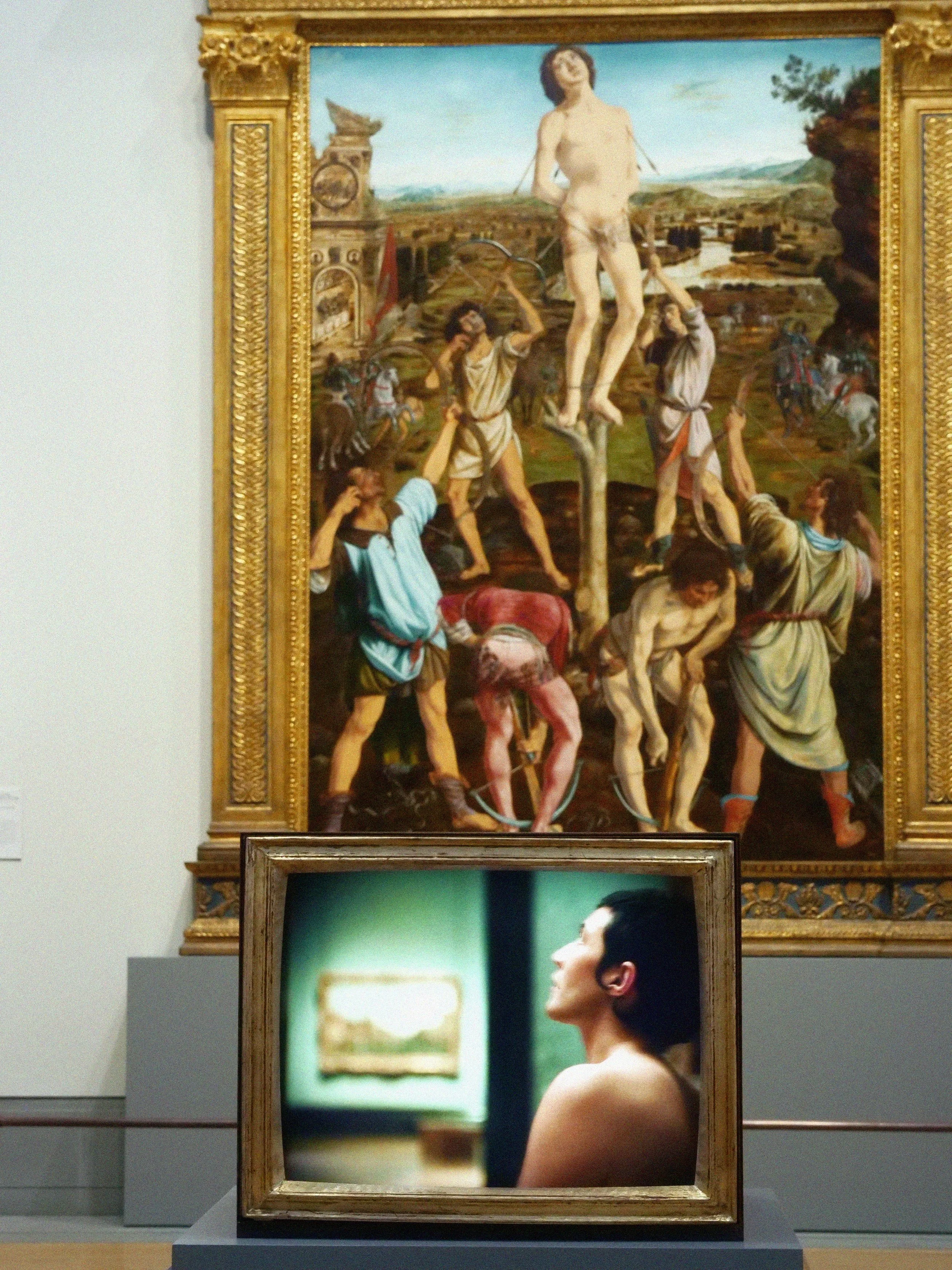 A framed painting depicting the crucifixion of Jesus Christ with people around it, and a modern photograph of a woman on display in front of it.