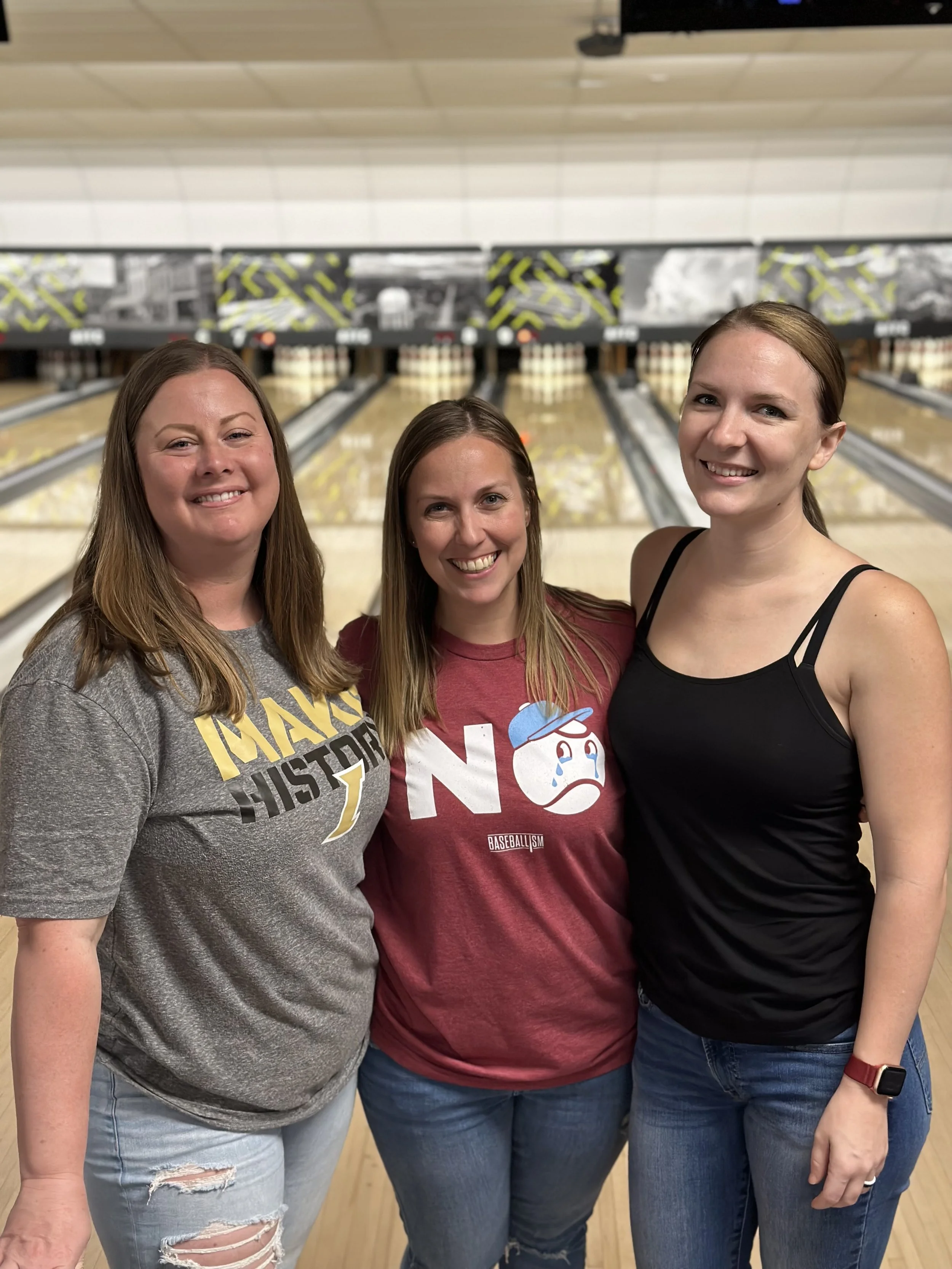 Three women standing together at a bowling alley, smiling for the camera.