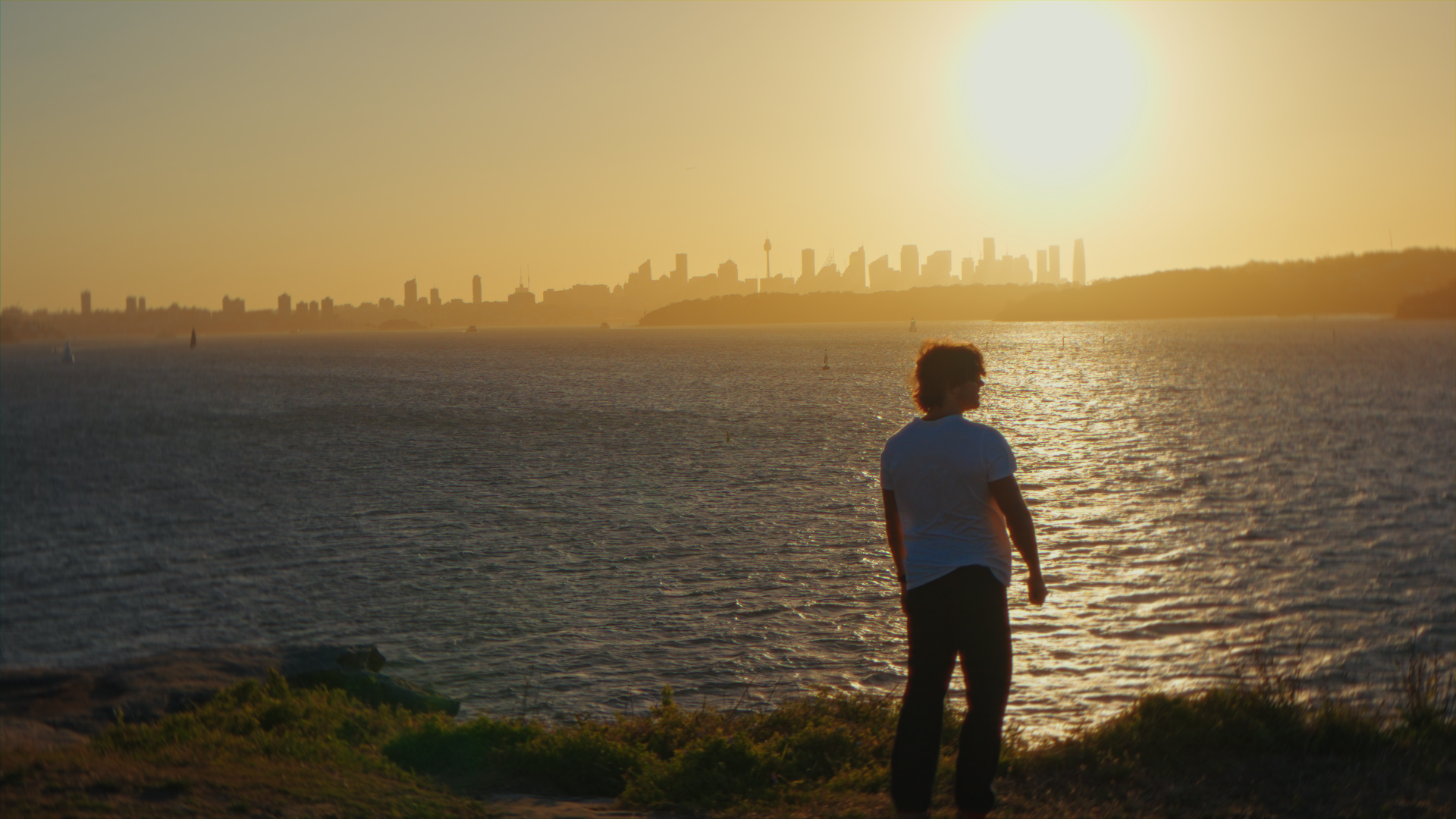 Persona che guarda il tramonto sul mare con lo skyline di una città sullo sfondo.