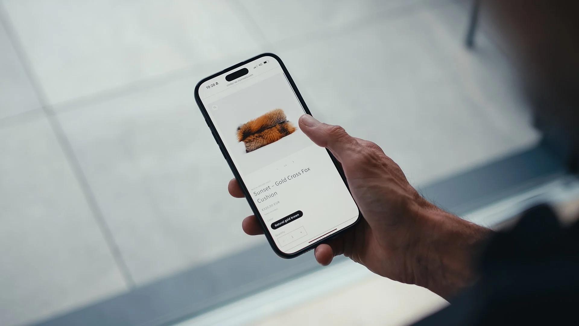 Una mano che tiene uno smartphone che mostra una calza di pelliccia marrone su uno schermo con prezzo e descrizione.