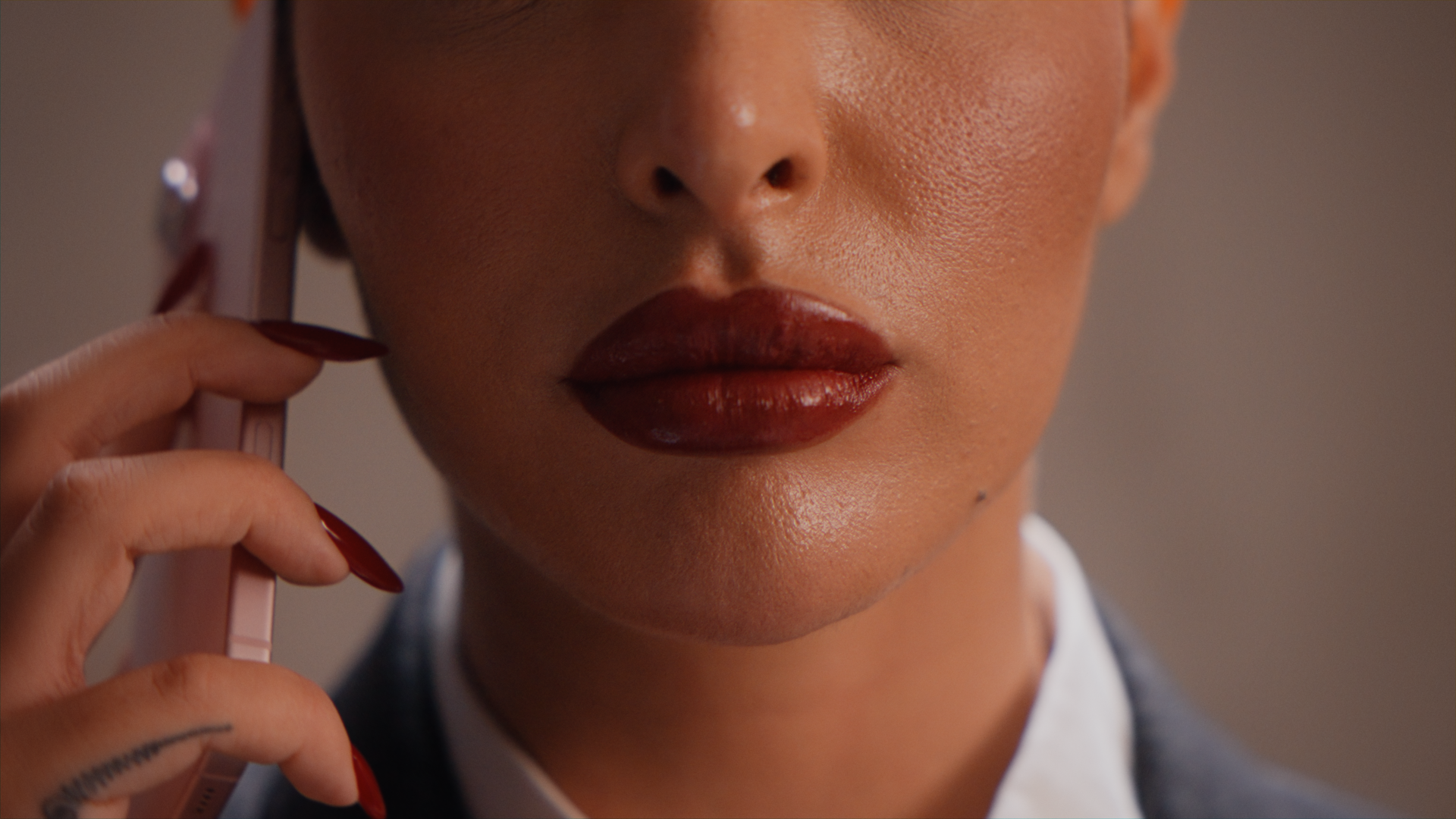 Primo piano di pria che tiene un telefono cellulare vicino all'orecchio, con labbra lucide e trucco evidente.