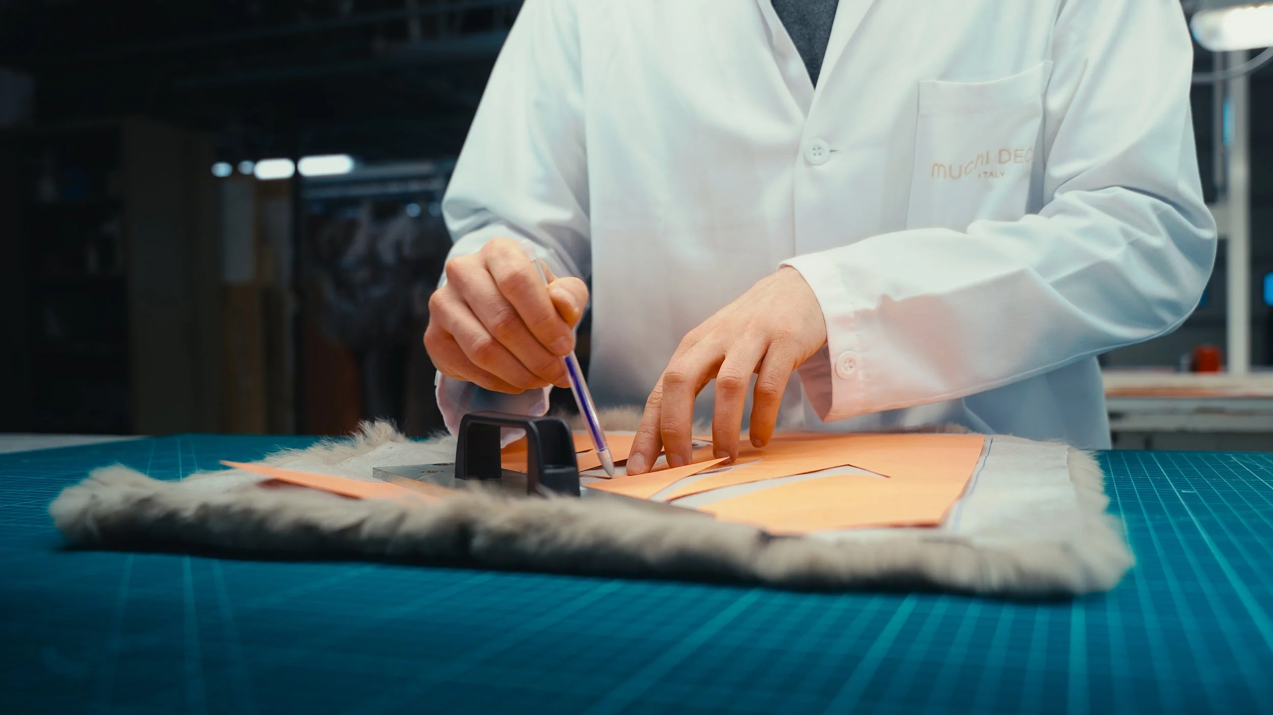 Persona in laboratorio che lavora sul disegno di un costume, con pelli di pelliccia sul tavolo.