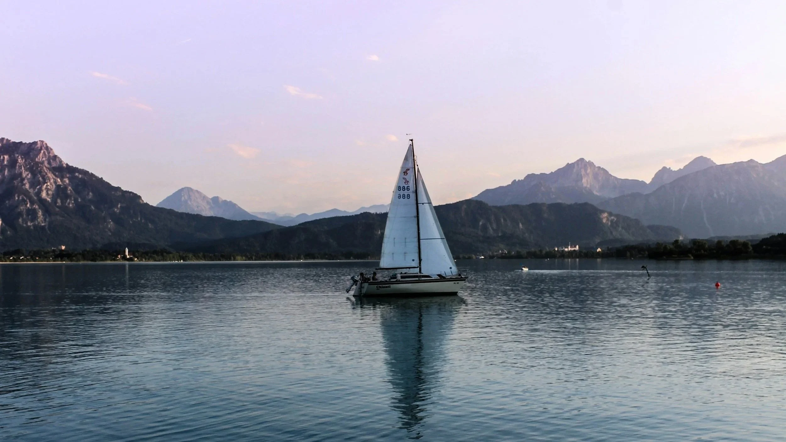 Una barca a vela su un lago con montagne sullo sfondo, cielo leggermente nuvoloso.