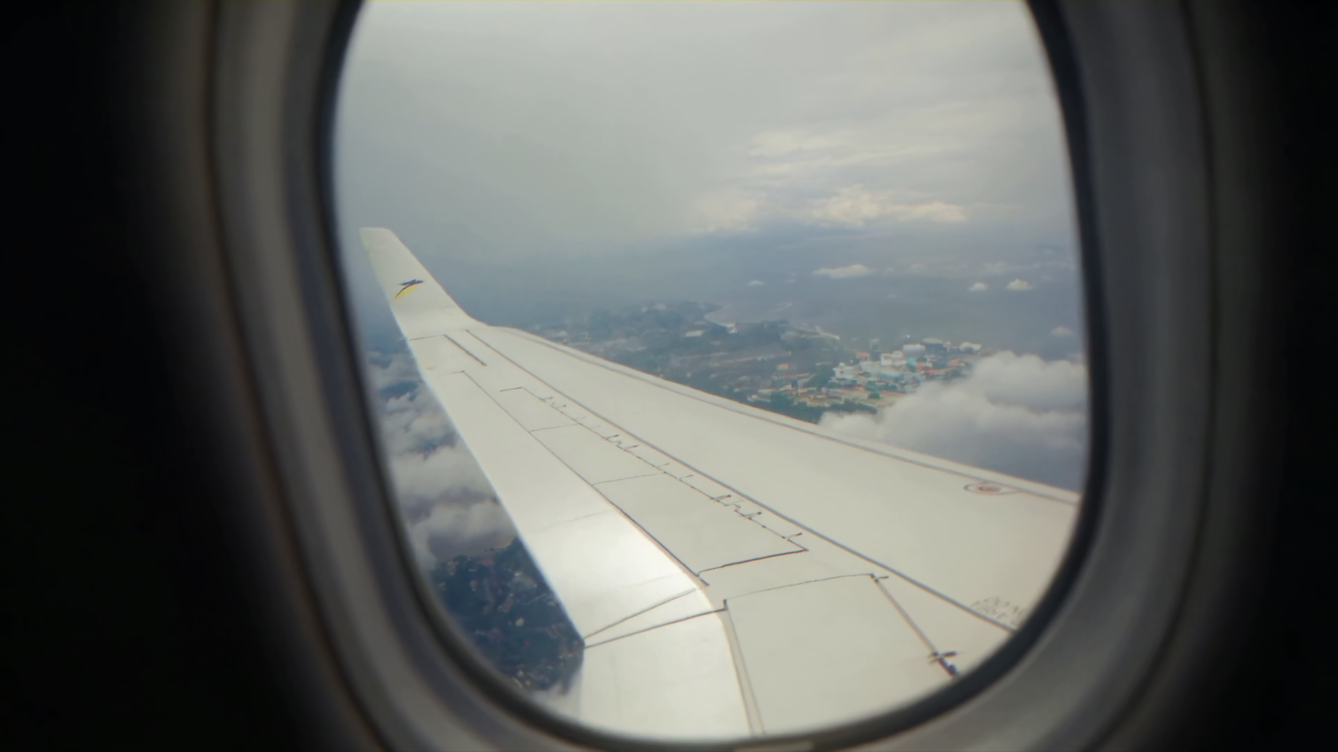 Vista dell'ala di un aereo vista attraverso la finestra, con paesaggi terrestri e nuvole sotto il volo.