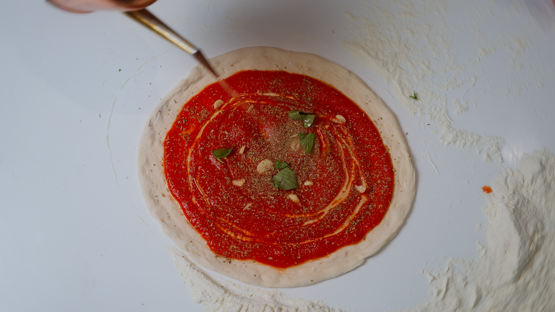 Preparazione di una pizza margherita con salsa di pomodoro, basilico e olio d'oliva su impasto crudo, con utensile da cucina sopra.