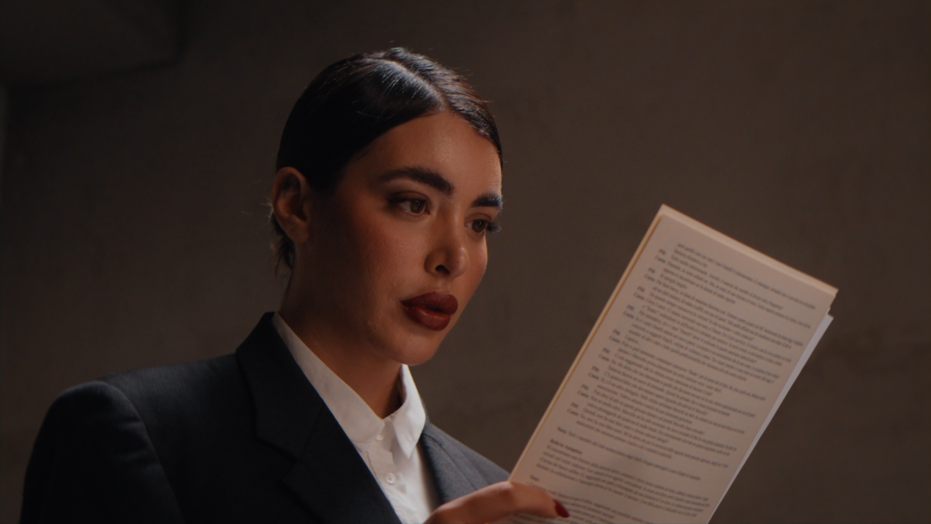 Donna con capelli scuri e trucco naturale, indossa un abbigliamento elegante e legge un documento