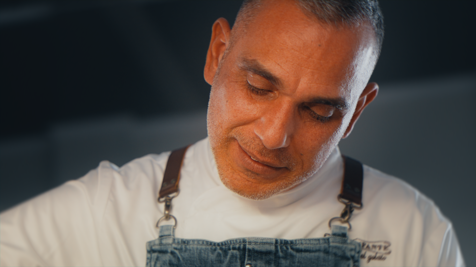 Chef uomo con capelli corti, stanco o concentrato, che indossa una giacca bianca e un grembiule di jeans.