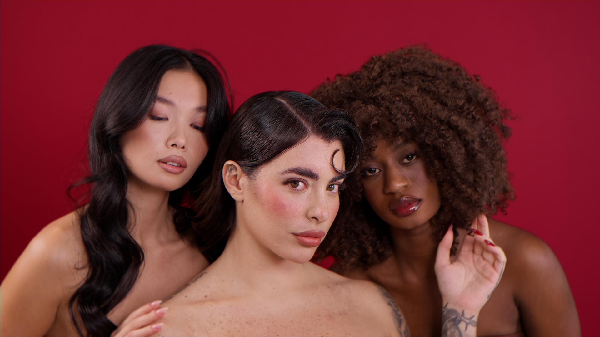 Tre donne con capelli ricci e lisci in posa contro uno sfondo rosso.