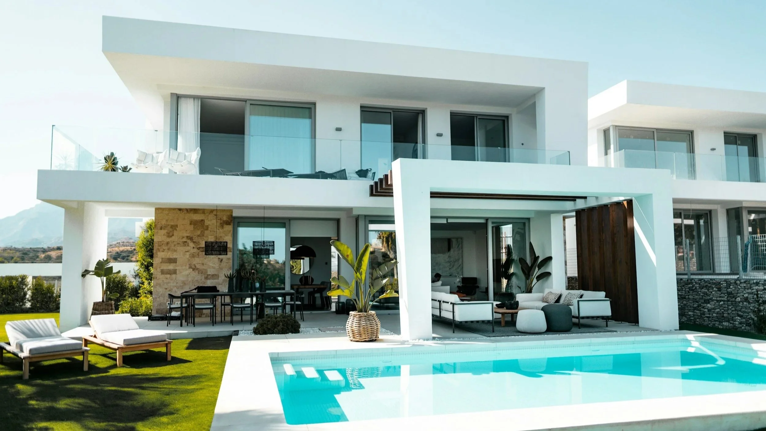 Villa moderna con piscina e area lounge all'aperto, balconi con vetri e zona giardino con lettini