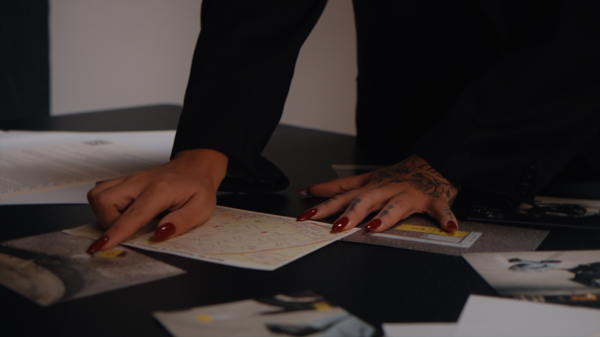 Mani con unghie rosse che lavorano su mappe e fotografie su un tavolo nero