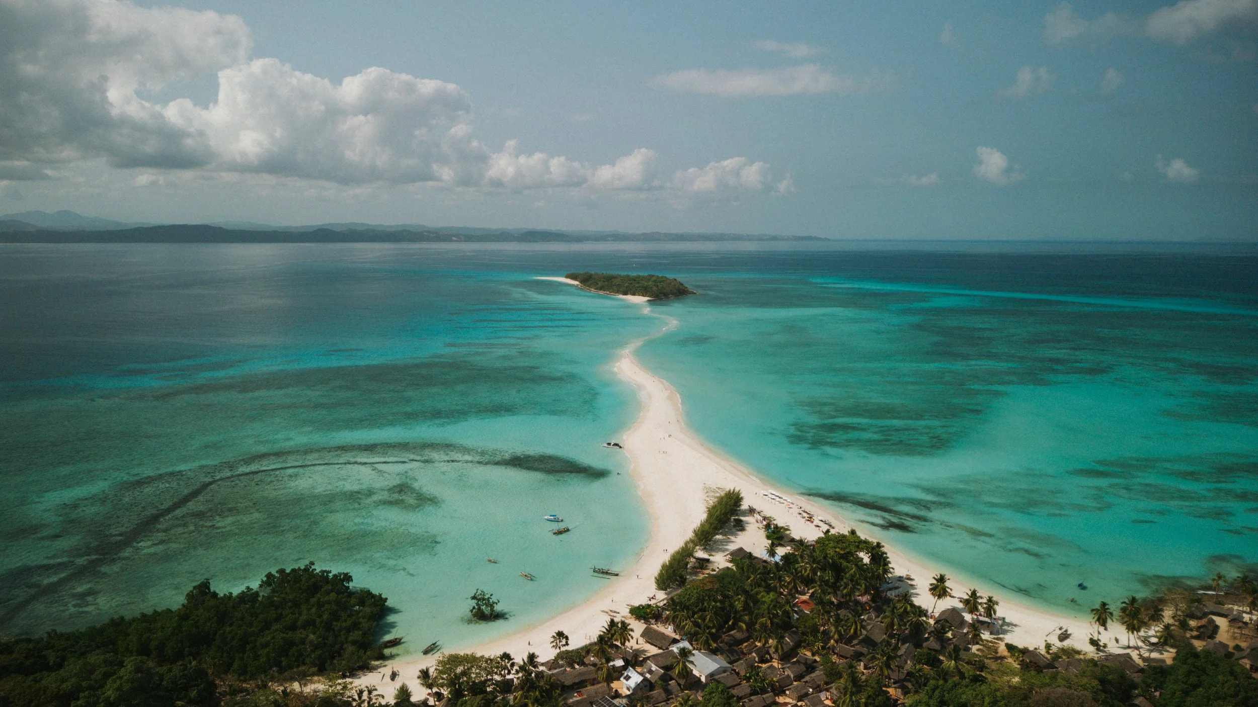 Spiaggia di sabbia bianca con acque turchesi, piccola isola al centro e villaggi con palme al lato