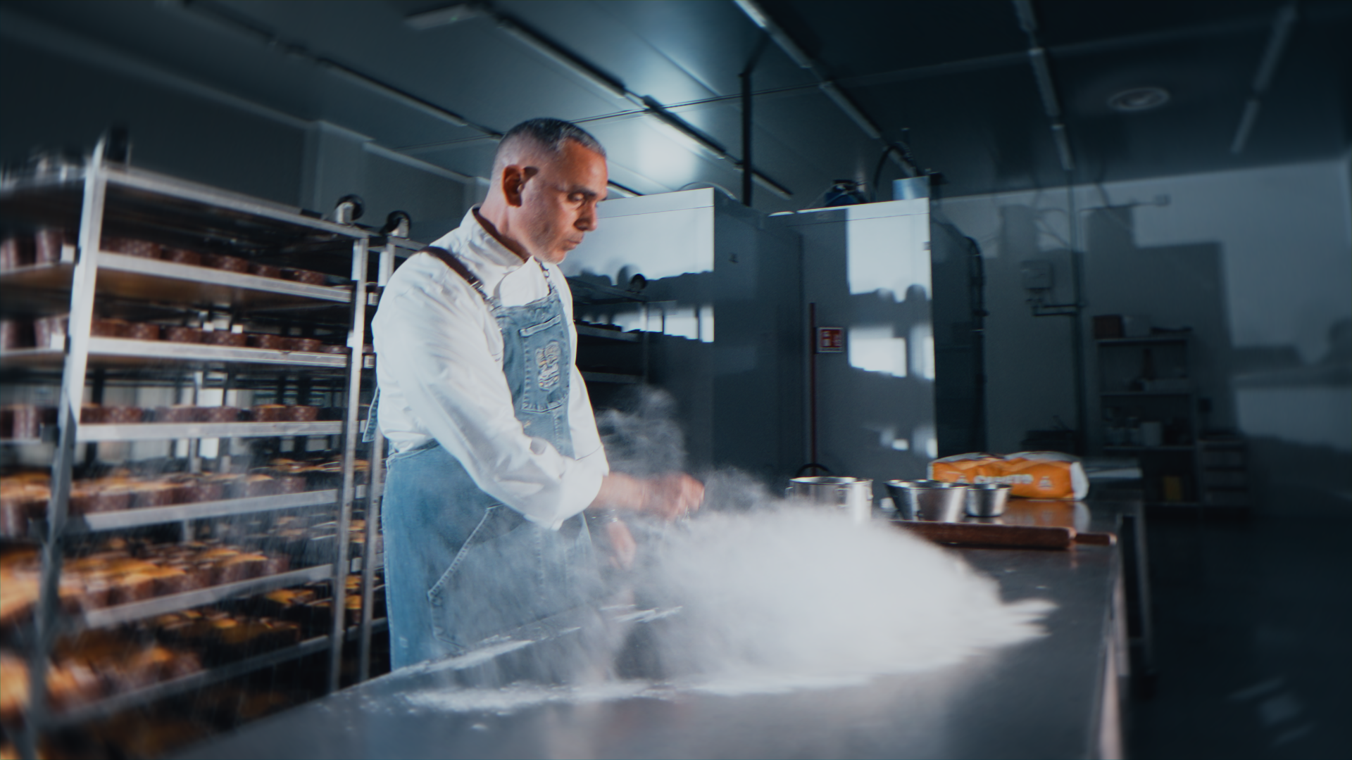 Chef in cucina con forno in background, che impiatta cibo mentre fuma.