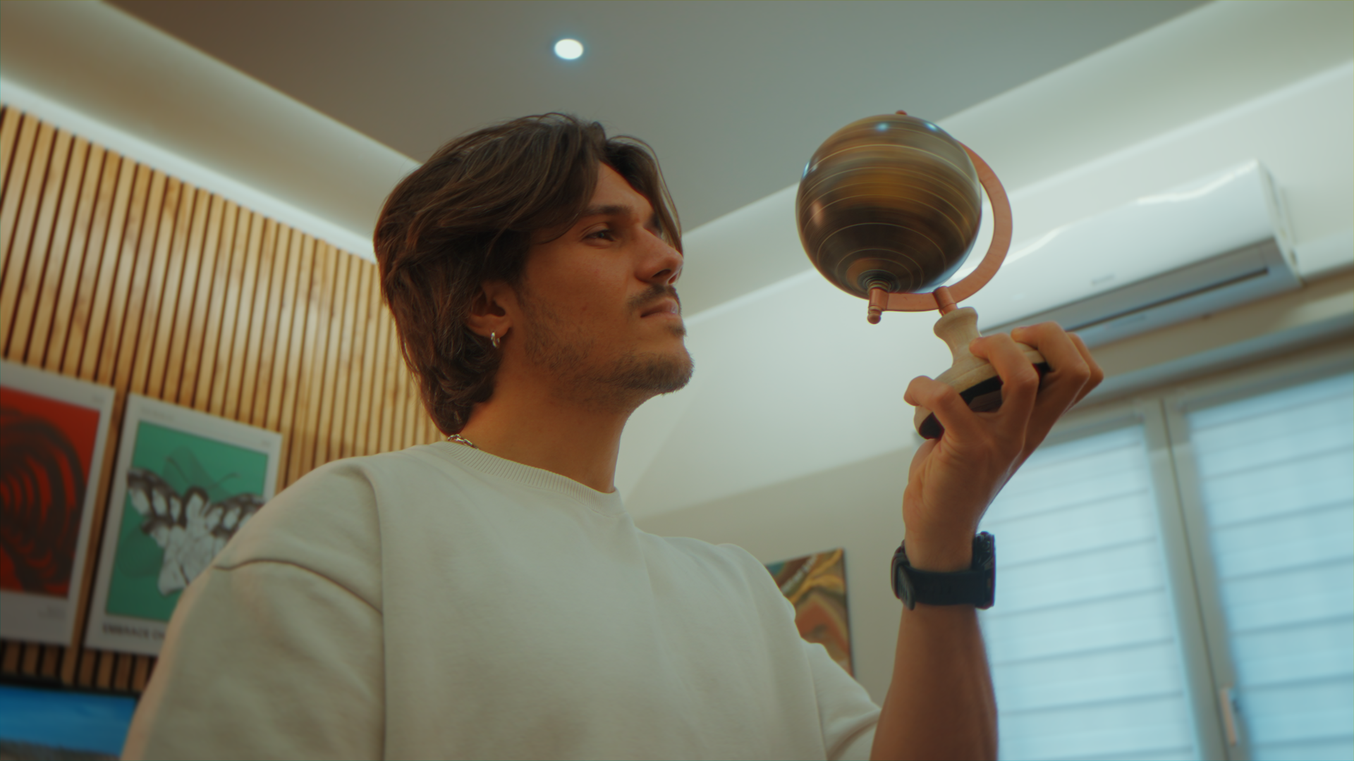 Un giovane uomo tiene in mano un planetario in miniatura in un ambiente moderno con pareti di legno e quadri alle pareti.