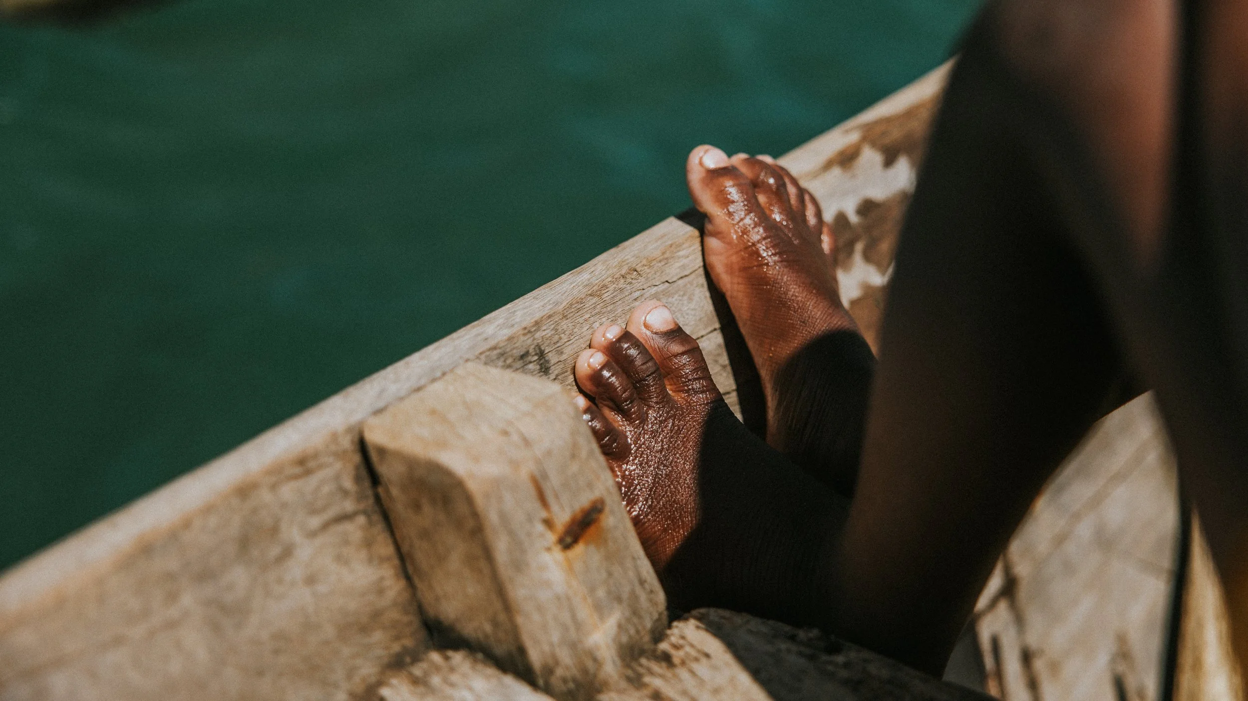 Mani bagnate che si appoggiano su una ringhiera di legno vicino all'acqua.