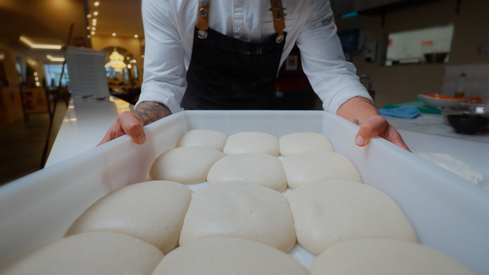 Uno chef che mostra pagnotte di pane lievitato su una teglia.