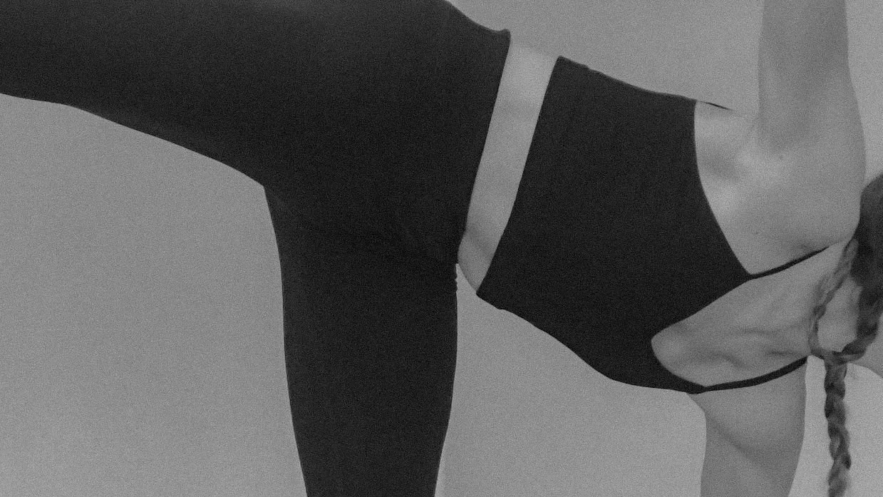 A person with a braid is doing a side plank pose in a black sports outfit and face mask.