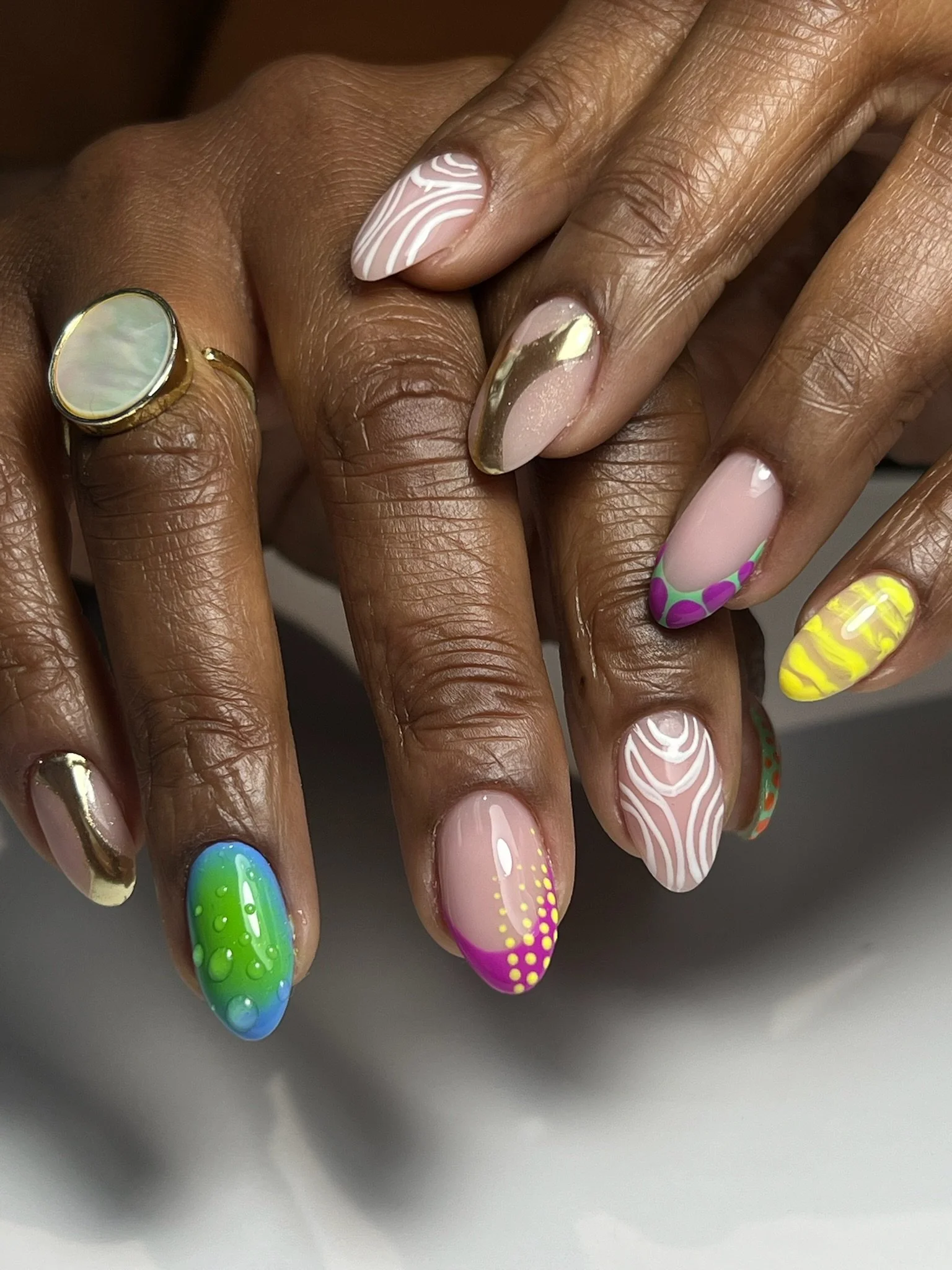 Close-up of hands with colorful, artistic nail designs featuring various patterns and colors, including abstract, dots, marbling, and gradient effects.