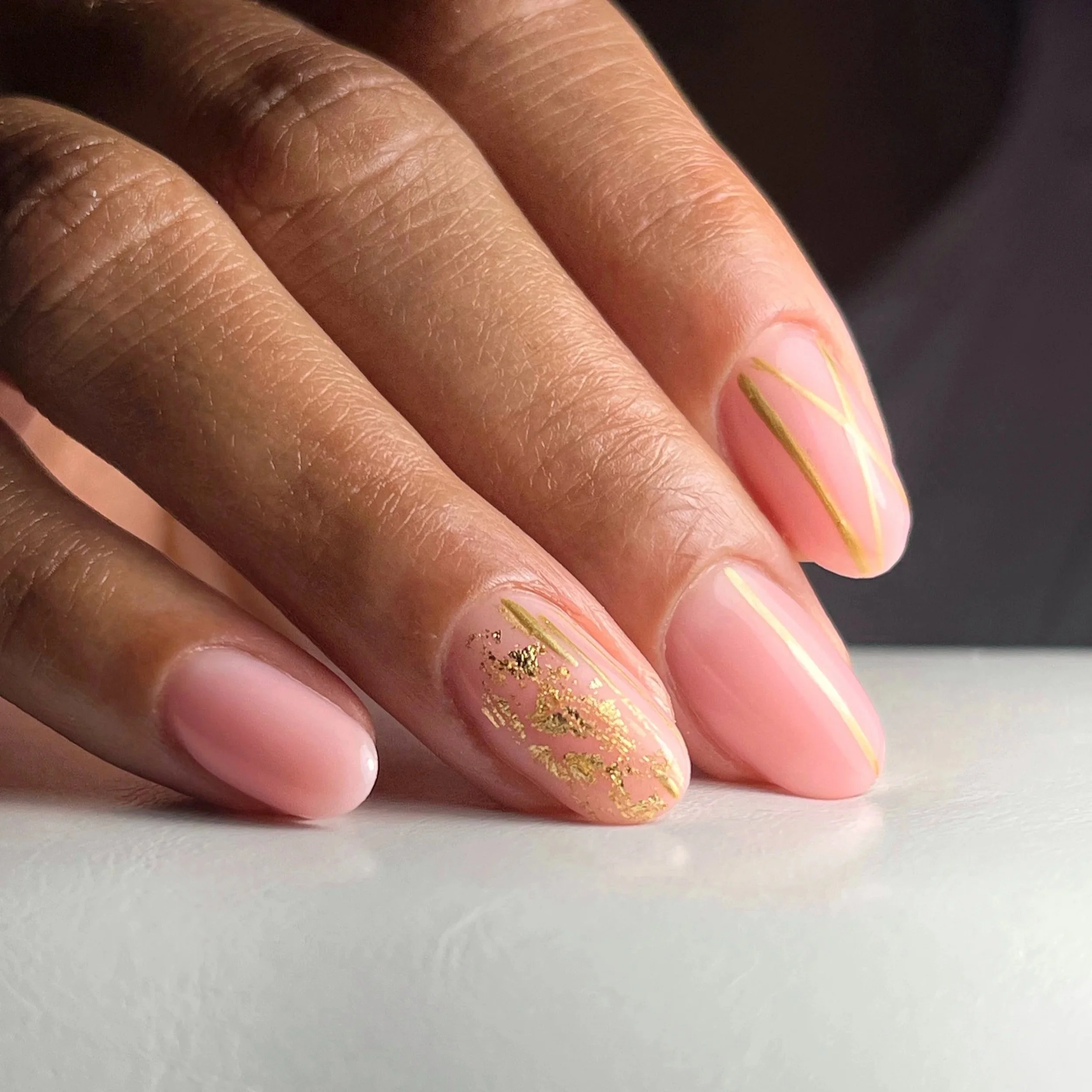 Close-up of a hand with pink and gold nail art, featuring gold foil accents on an oval-shaped fingernail.