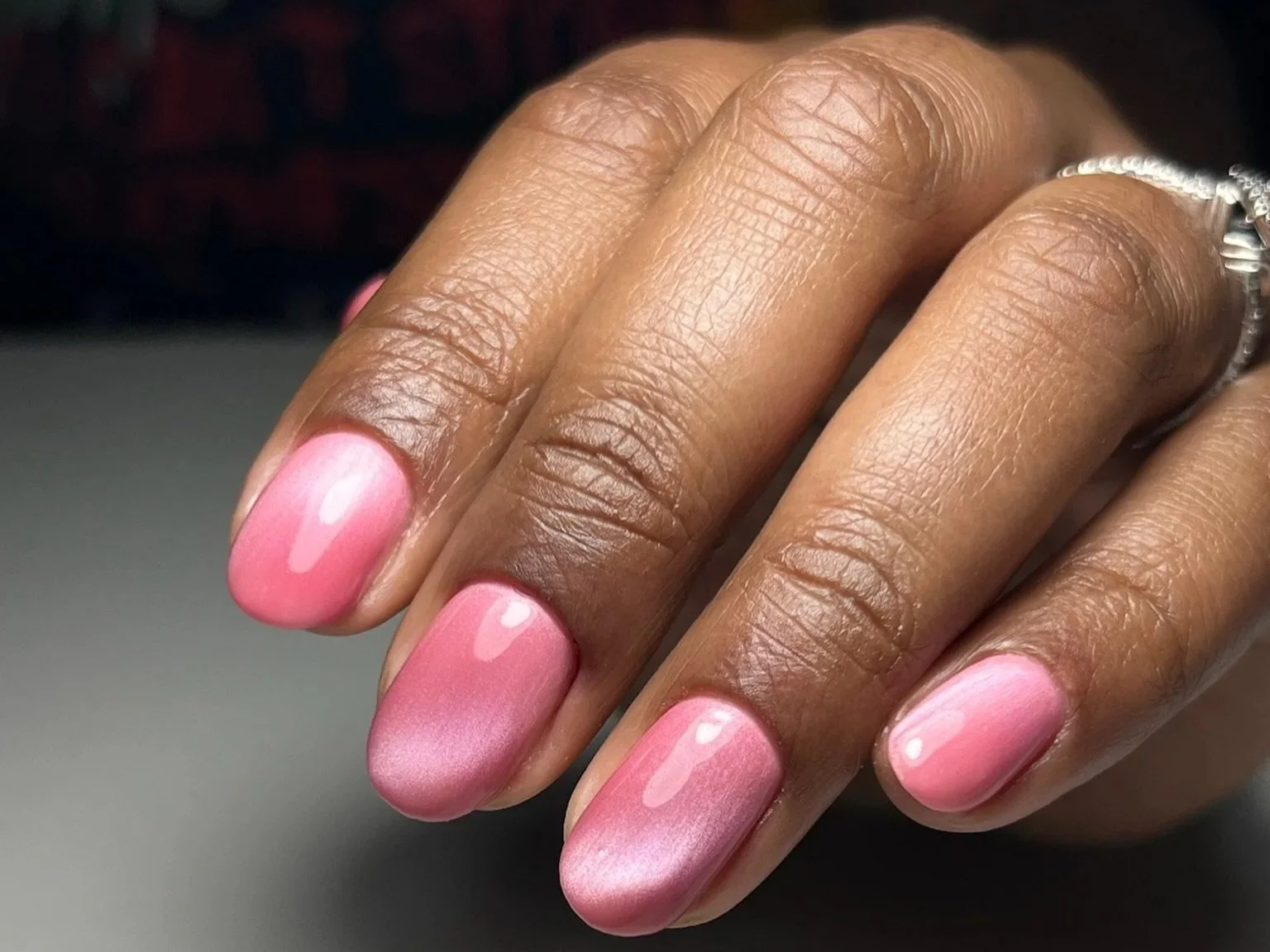 Close-up of a woman's hand with pink, shiny, nail polish on fingernails, wearing a silver ring on ring finger.