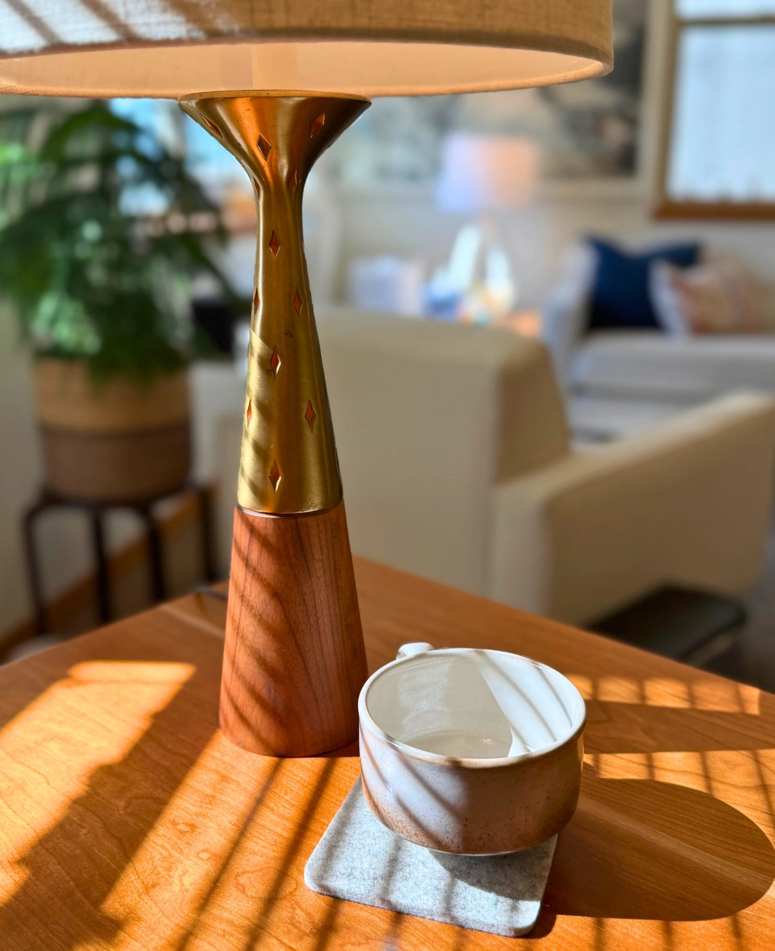 A wooden table with a tall, vintage-style lamp and empty ceramic cup in sunlight casting shadows.