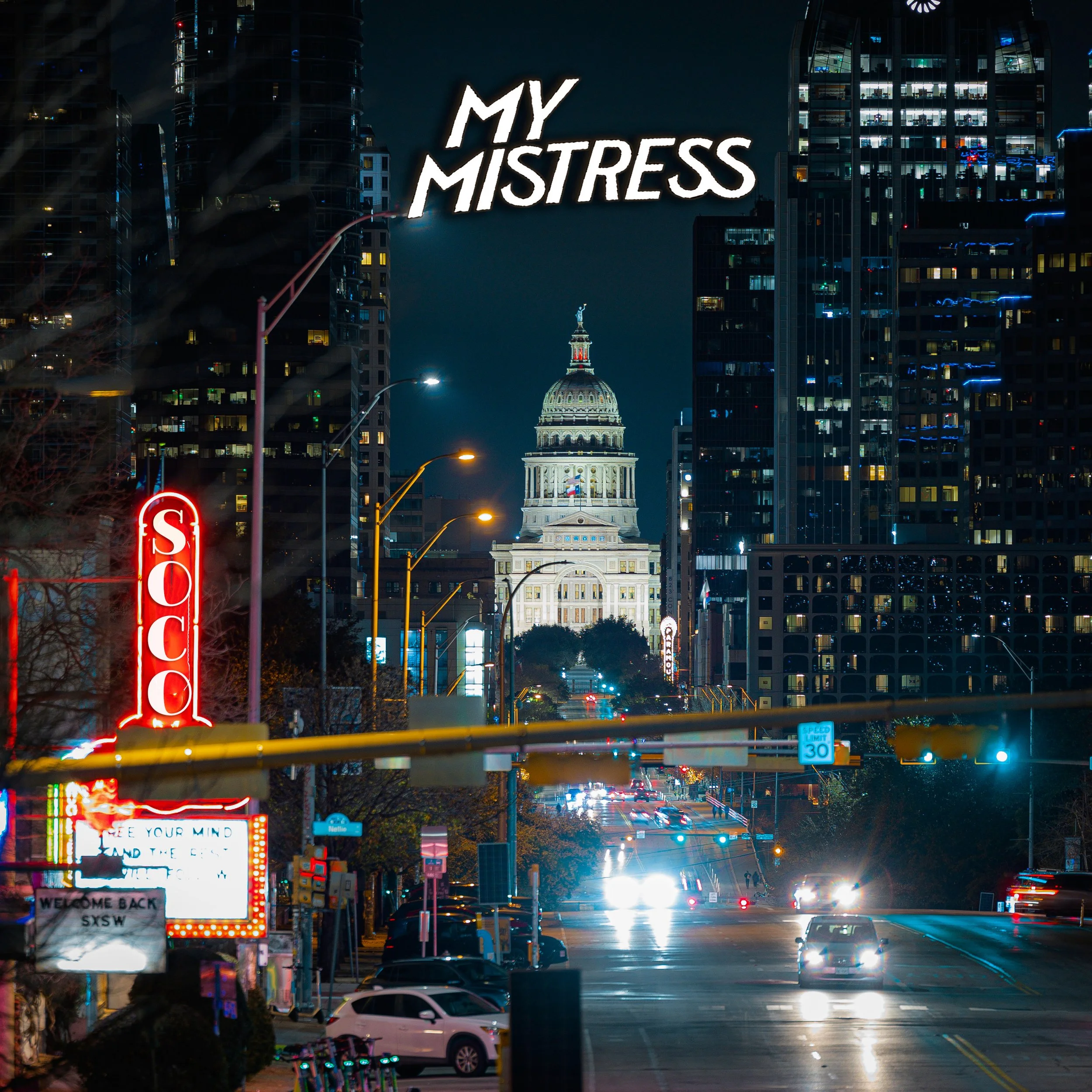 City street at night with illuminated signs, tall buildings, and the Texas State Capitol building in the background. Traffic and streetlights are visible. Soco Album cover  Chace Levi Lacey Kay Levi Geoff Garcia