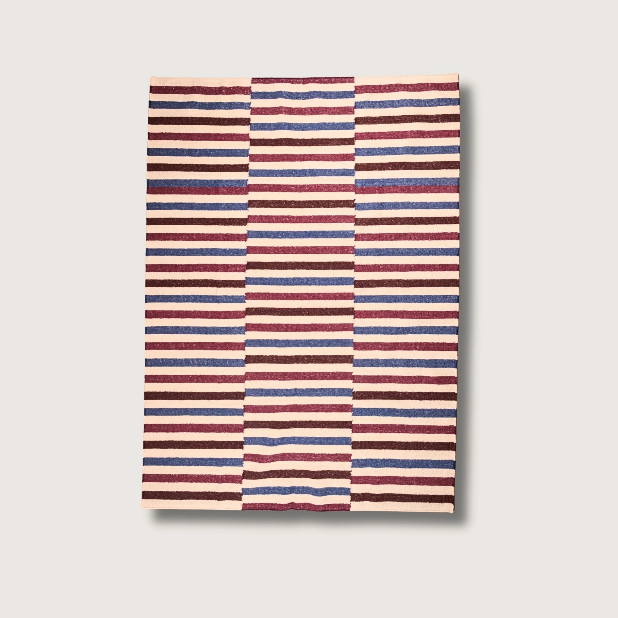 Saanjh handwoven striped wool rug with red, brown and blue tones on a natural base, flatweave design