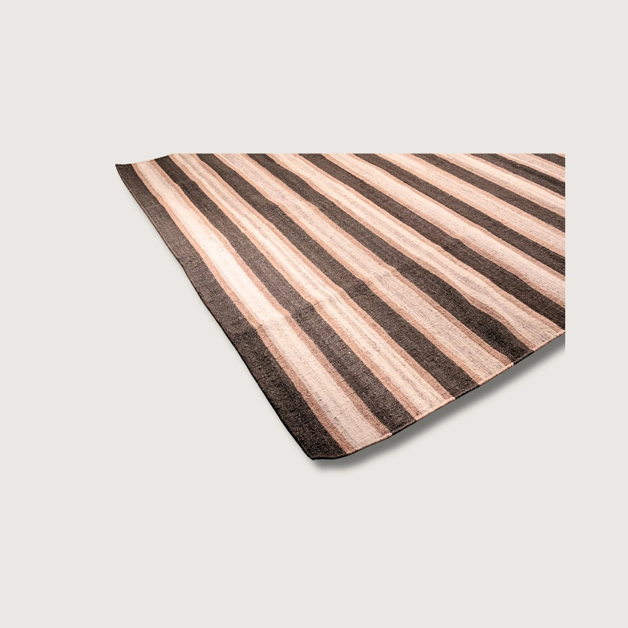 Angled view of Dhaariya Mitti rug with earthy stripe detail and natural wool texture