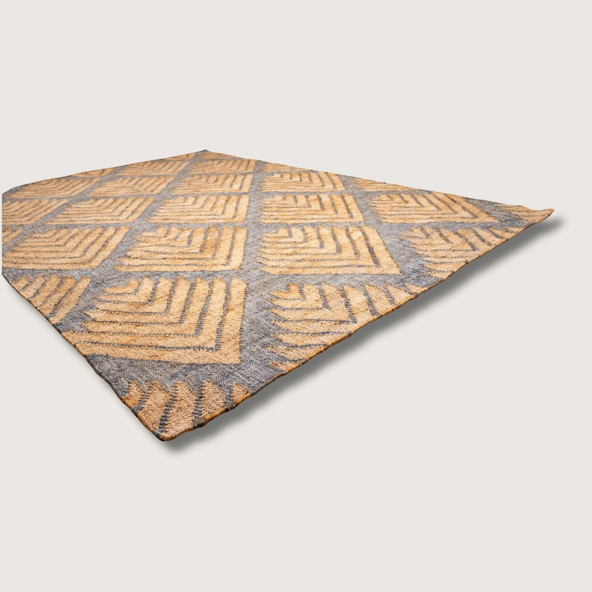 Handwoven jute rug with textured palm-inspired geometric pattern in natural sand and muted blue-grey tones.
