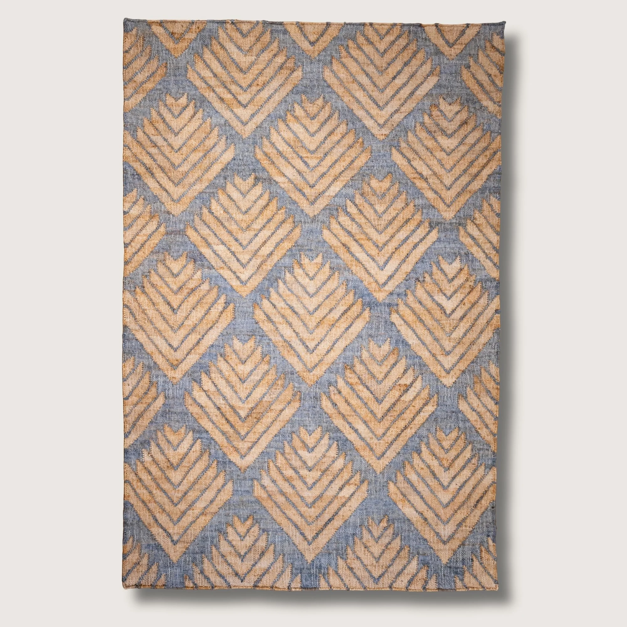 Handwoven jute rug with textured palm-inspired geometric pattern in natural sand and muted blue-grey tones.