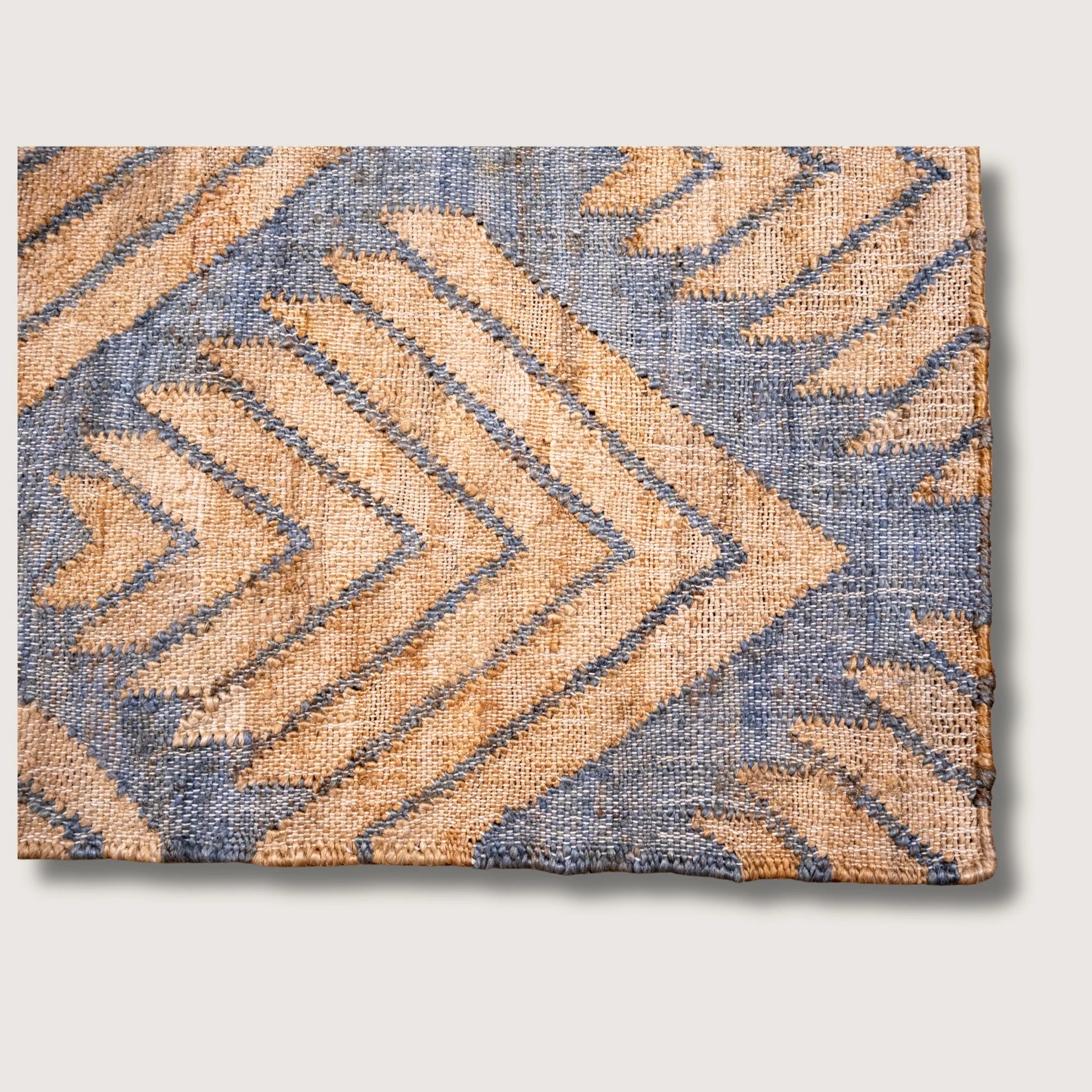 Handwoven jute rug with textured palm-inspired geometric pattern in natural sand and muted blue-grey tones.