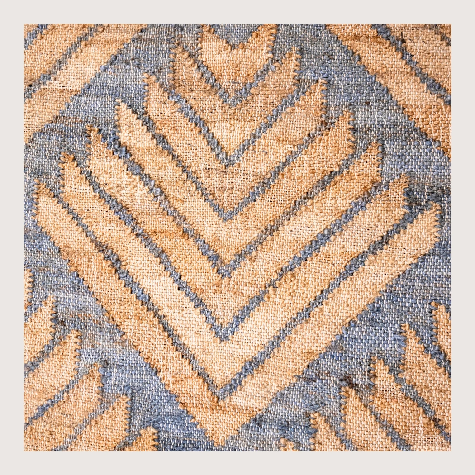 Handwoven jute rug with textured palm-inspired geometric pattern in natural sand and muted blue-grey tones.