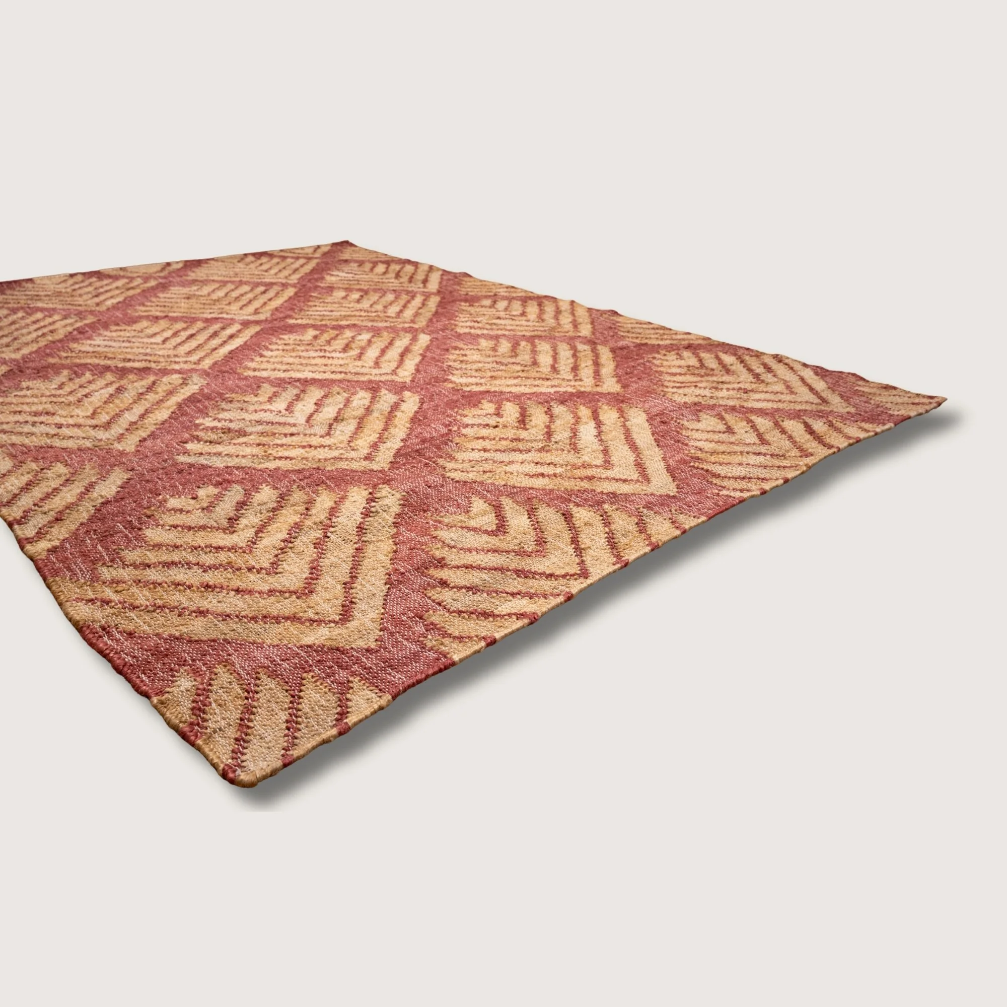 Handwoven jute rug with textured palm-inspired geometric pattern in dusty gulabi and natural sand tones.