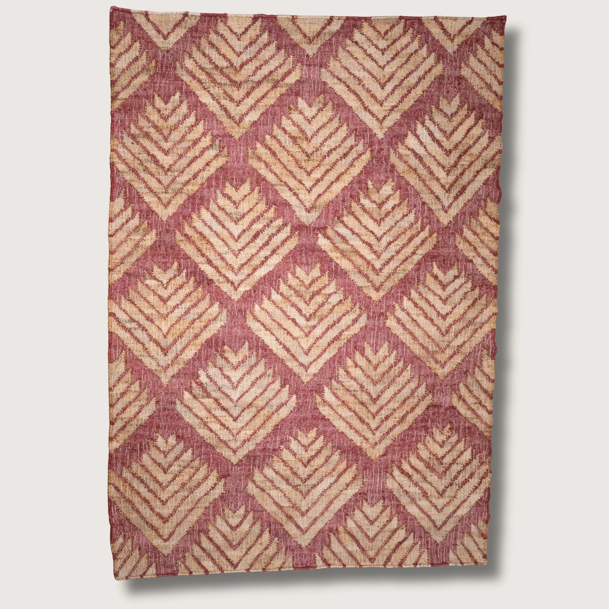 Handwoven jute rug with textured palm-inspired geometric pattern in dusty gulabi and natural sand tones.