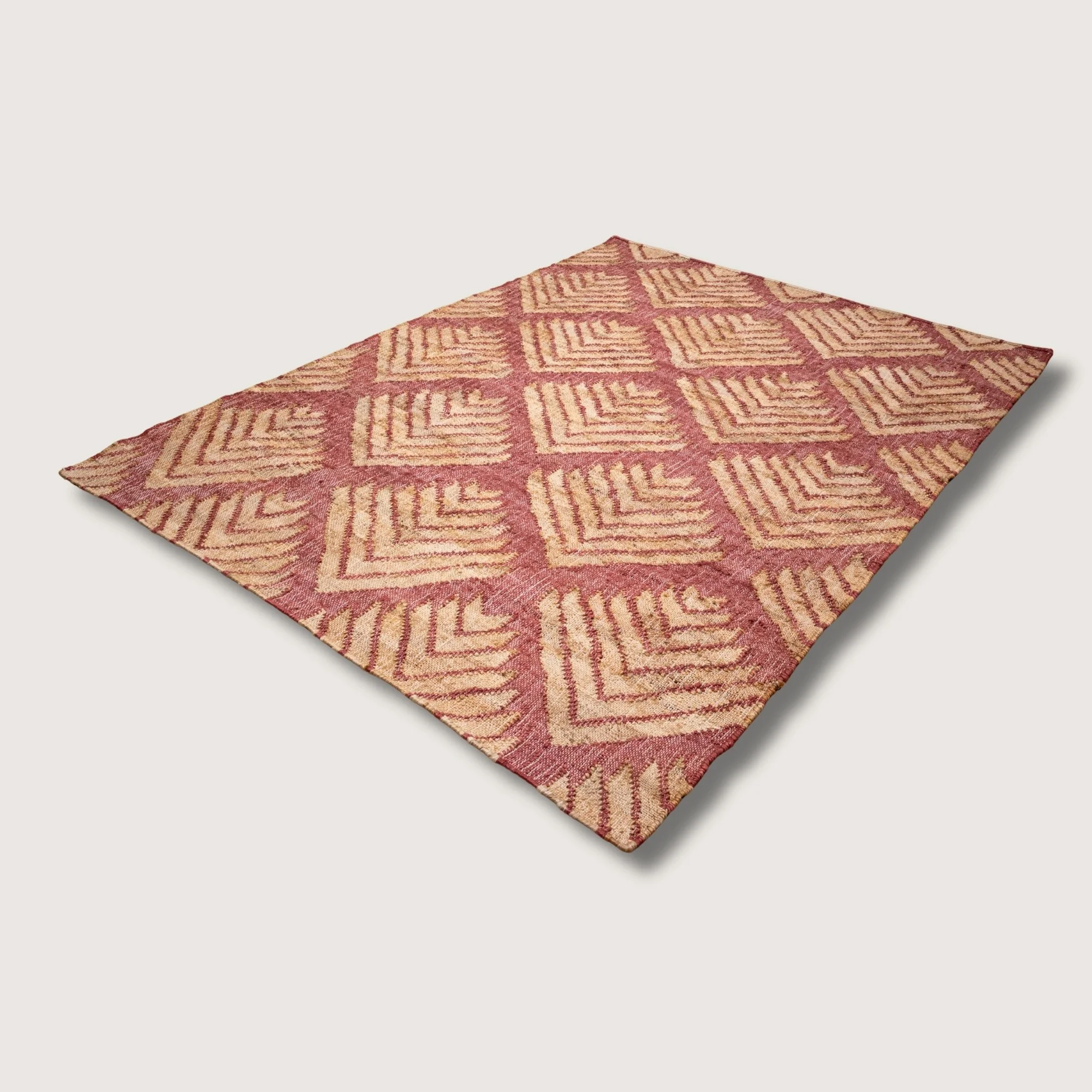 Handwoven jute rug with textured palm-inspired geometric pattern in dusty gulabi and natural sand tones.