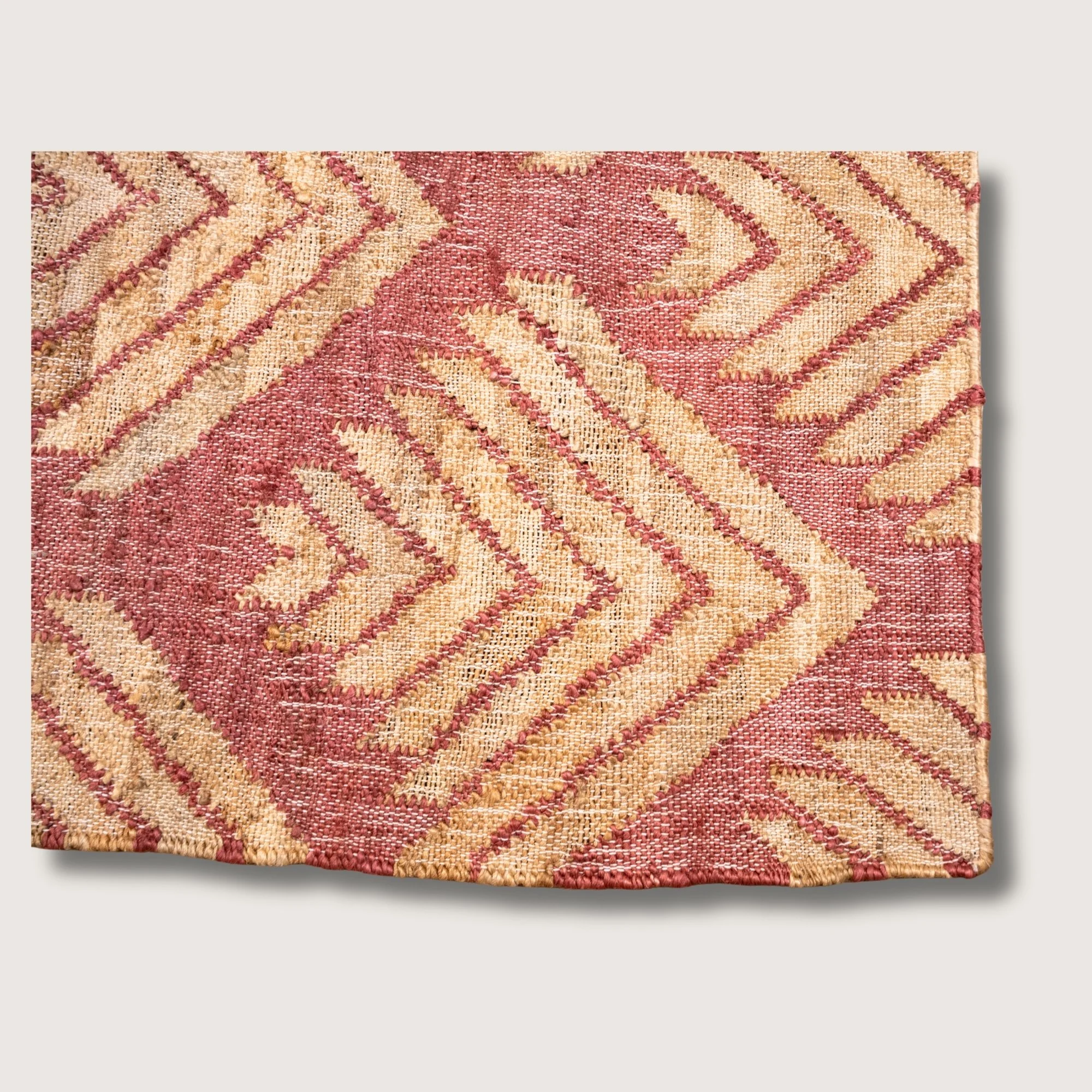 Handwoven jute rug with textured palm-inspired geometric pattern in dusty gulabi and natural sand tones.
