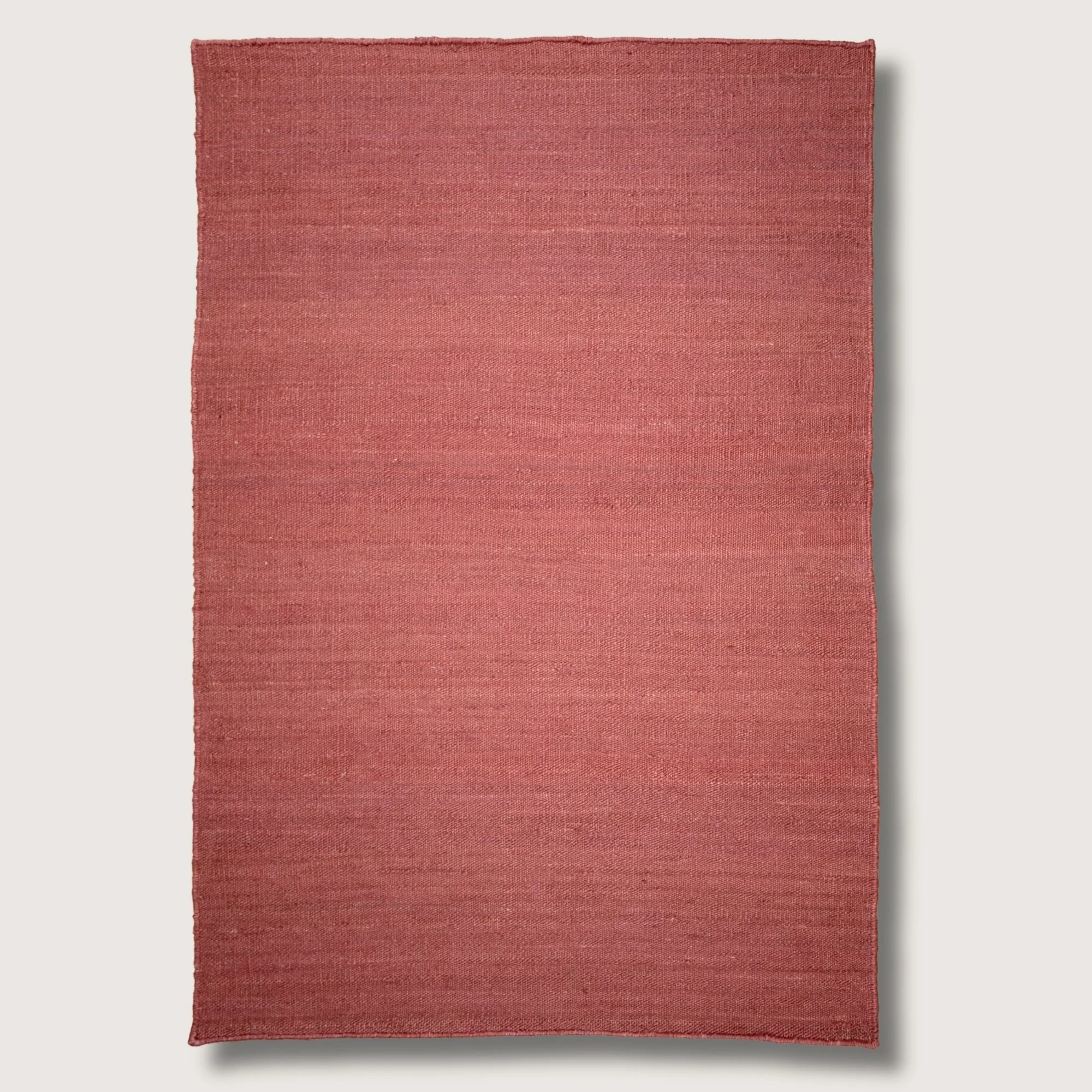 Plain handwoven jute rug in soft dusty gulabi tones with subtle natural texture.