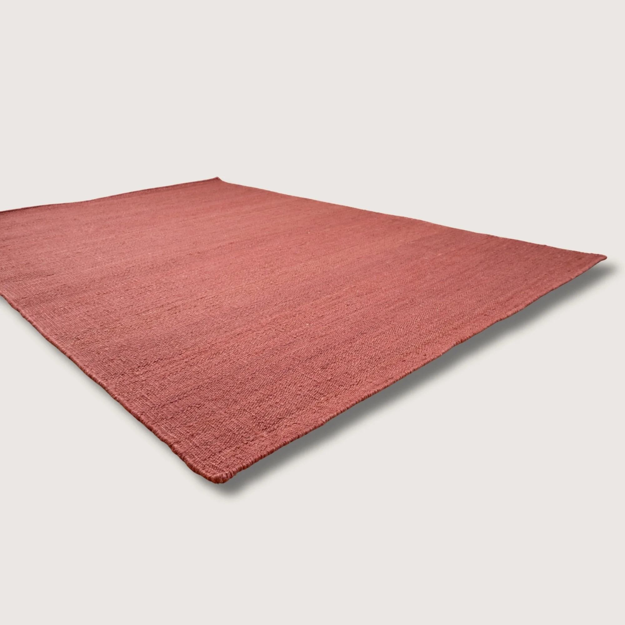 Plain handwoven jute rug in soft dusty gulabi tones with subtle natural texture.