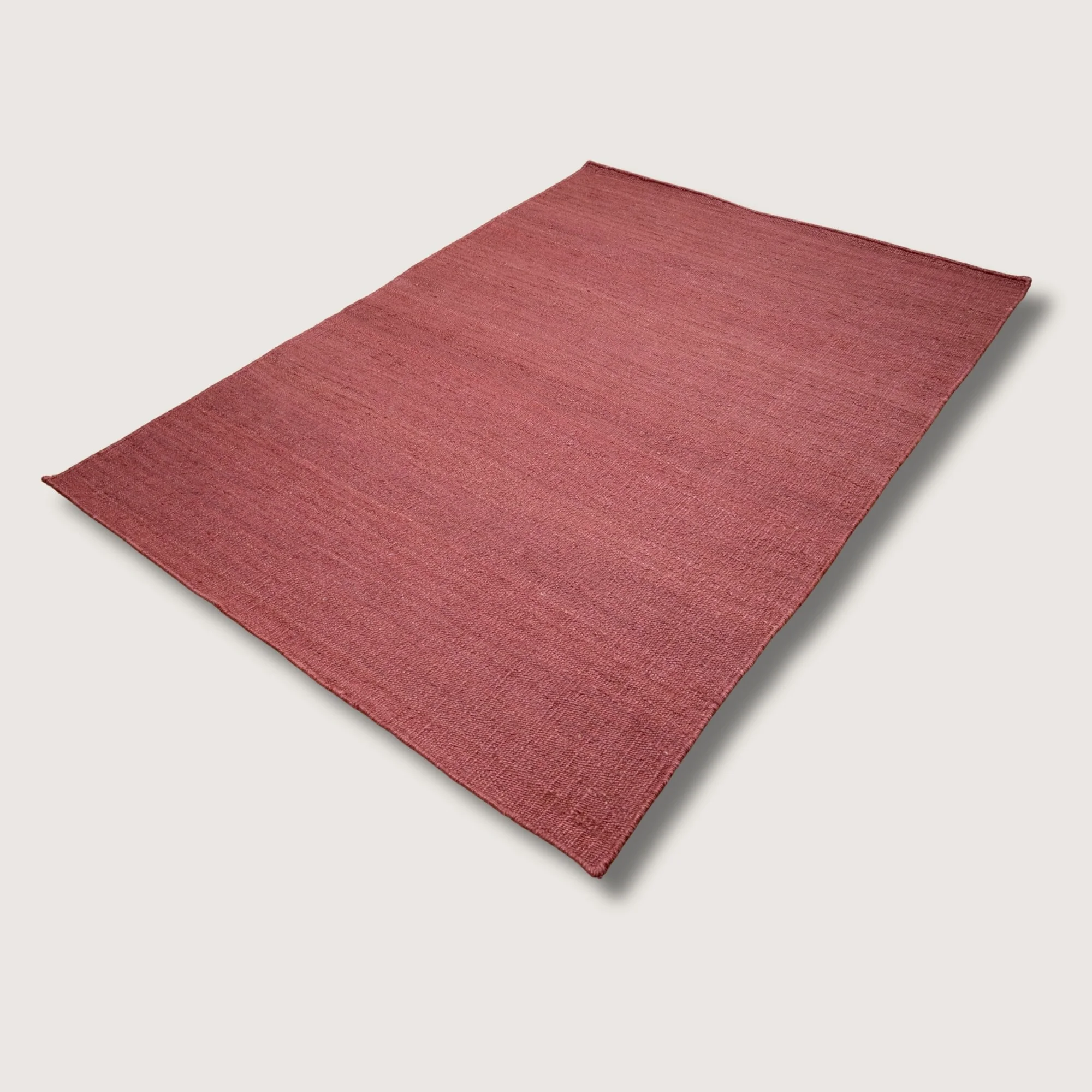 Plain handwoven jute rug in soft dusty gulabi tones with subtle natural texture.