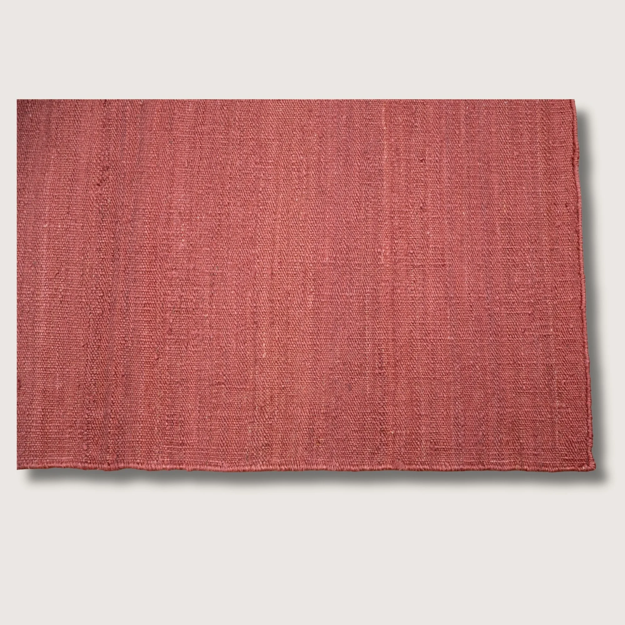 Plain handwoven jute rug in soft dusty gulabi tones with subtle natural texture.