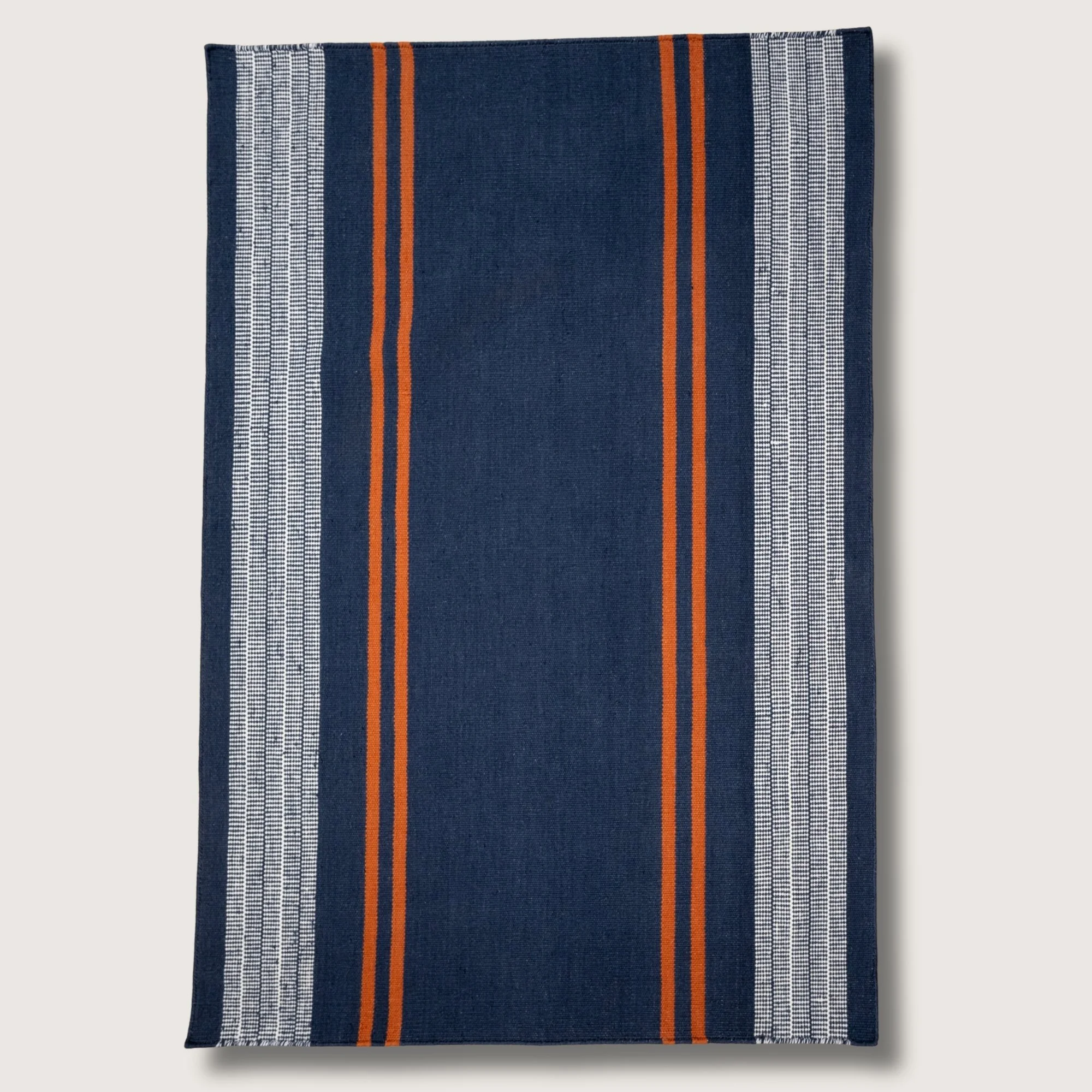 Handwoven wool flatweave rug with striped pattern in deep neel, whisper white, and Bombay brown tones.