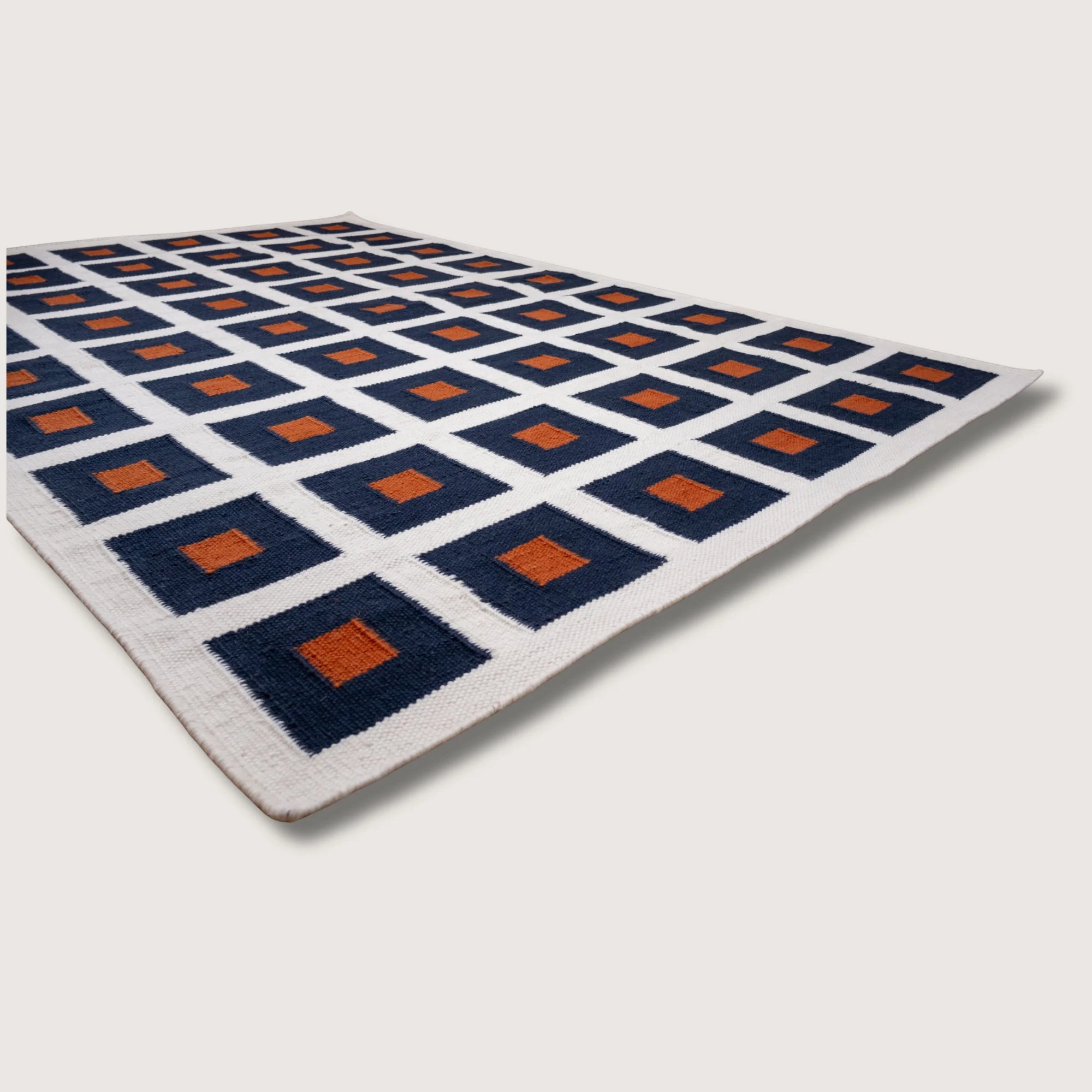 Handwoven wool flatweave rug with geometric square pattern in deep neel, whisper white, and Bombay brown tones.