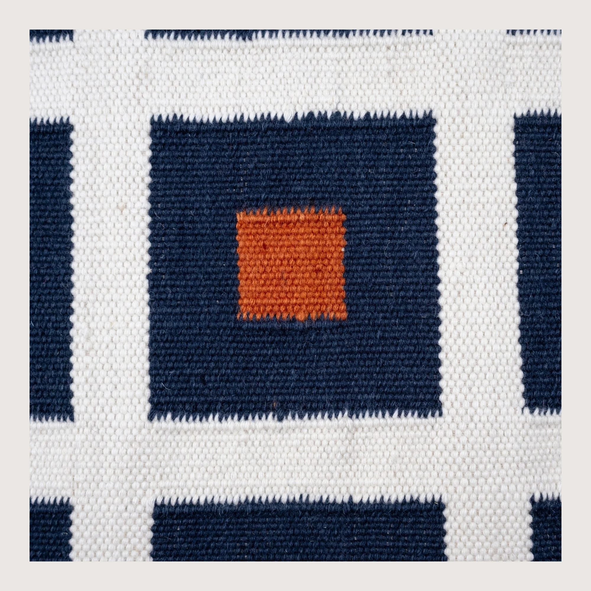 Handwoven wool flatweave rug with geometric square pattern in deep neel, whisper white, and Bombay brown tones.