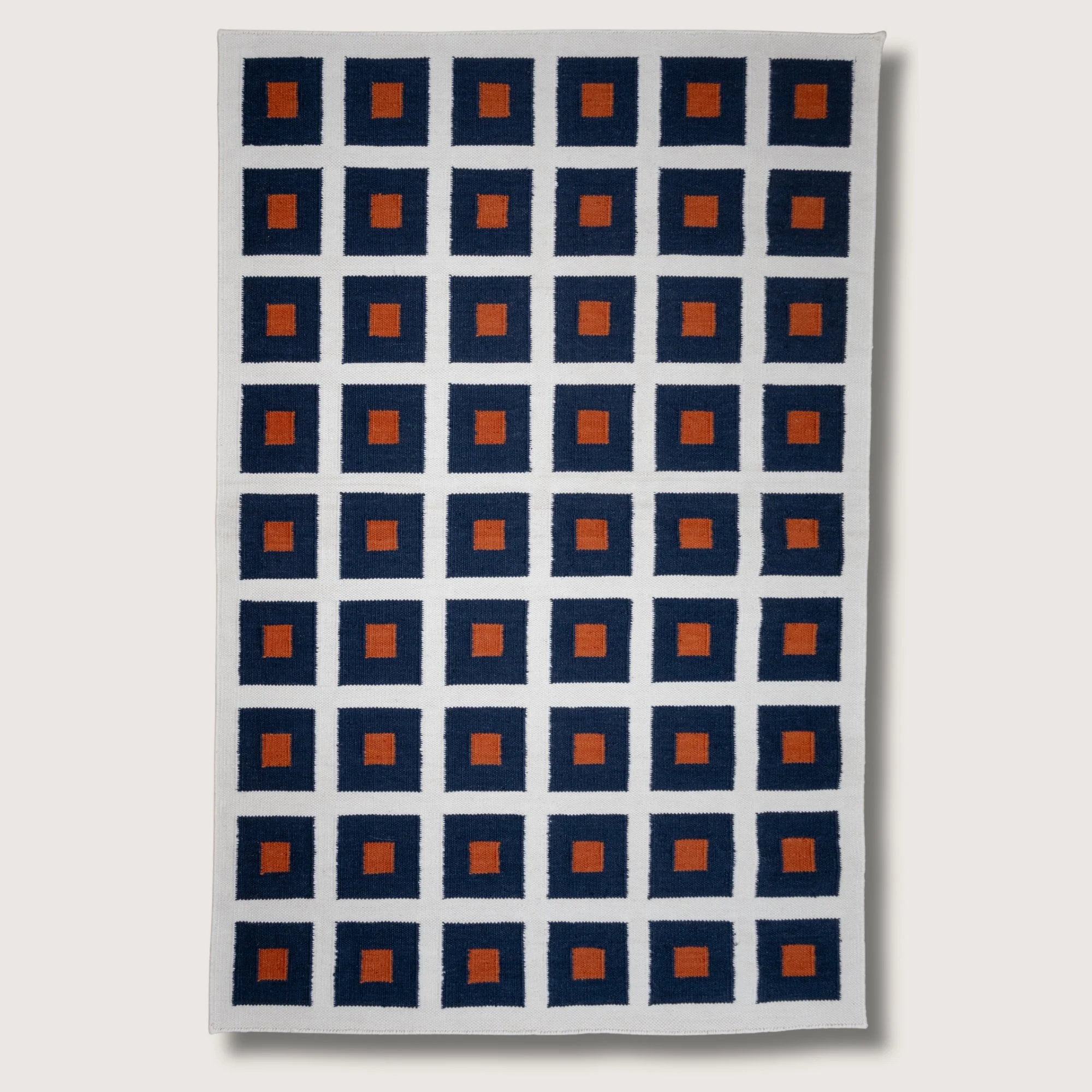 Handwoven wool flatweave rug with geometric square pattern in deep neel, whisper white, and Bombay brown tones.
