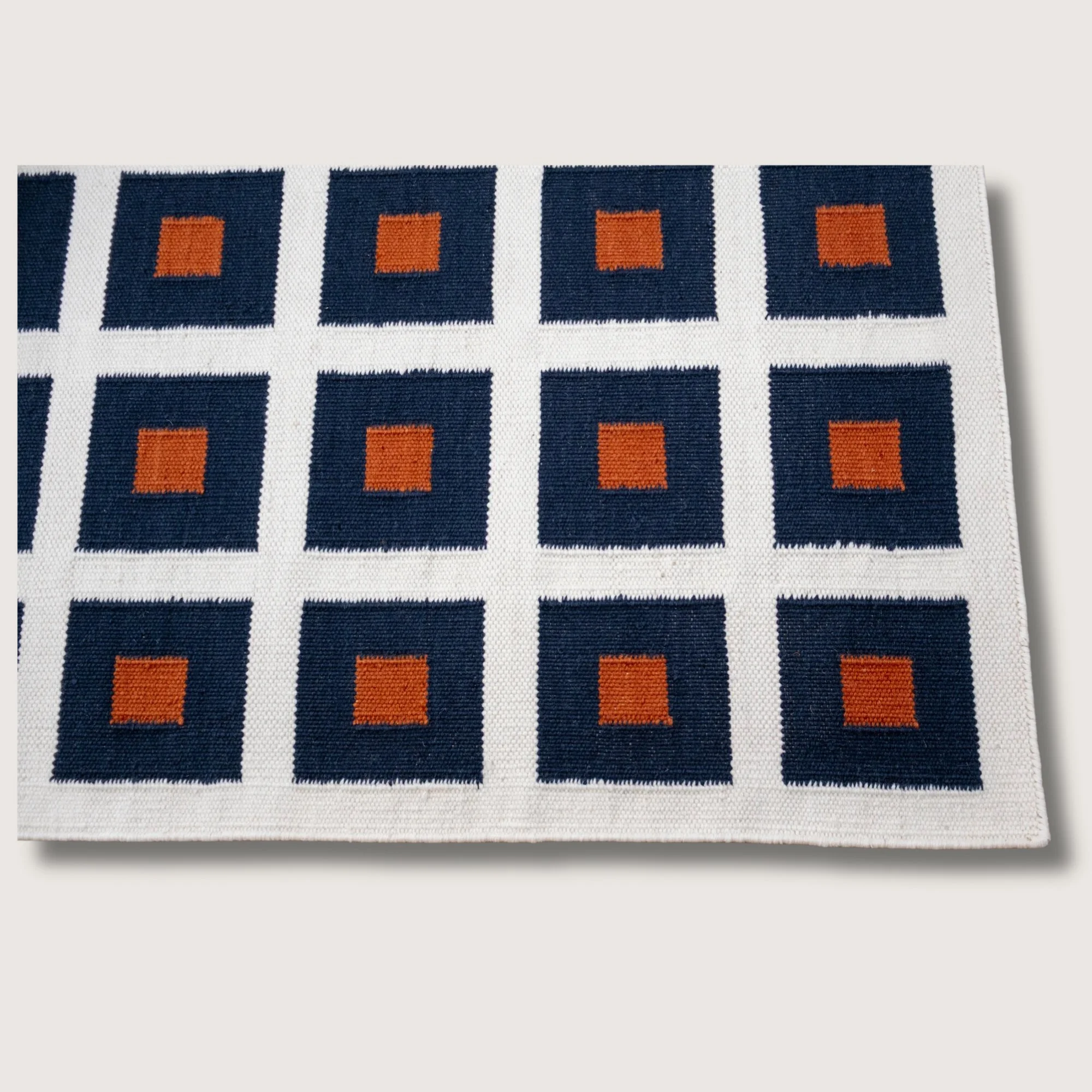 Handwoven wool flatweave rug with geometric square pattern in deep neel, whisper white, and Bombay brown tones.