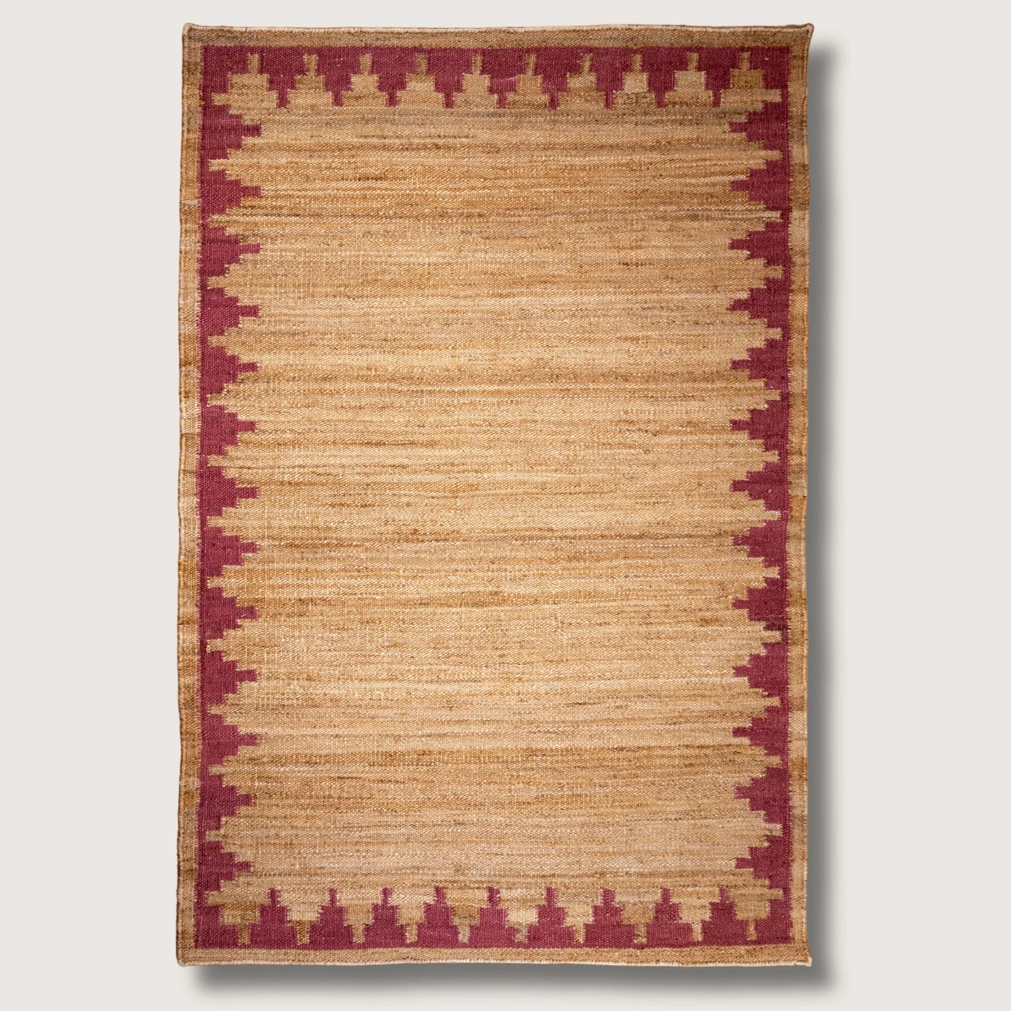 Handwoven jute rug with stepped geometric border in dusty gulabi and natural sand tones.