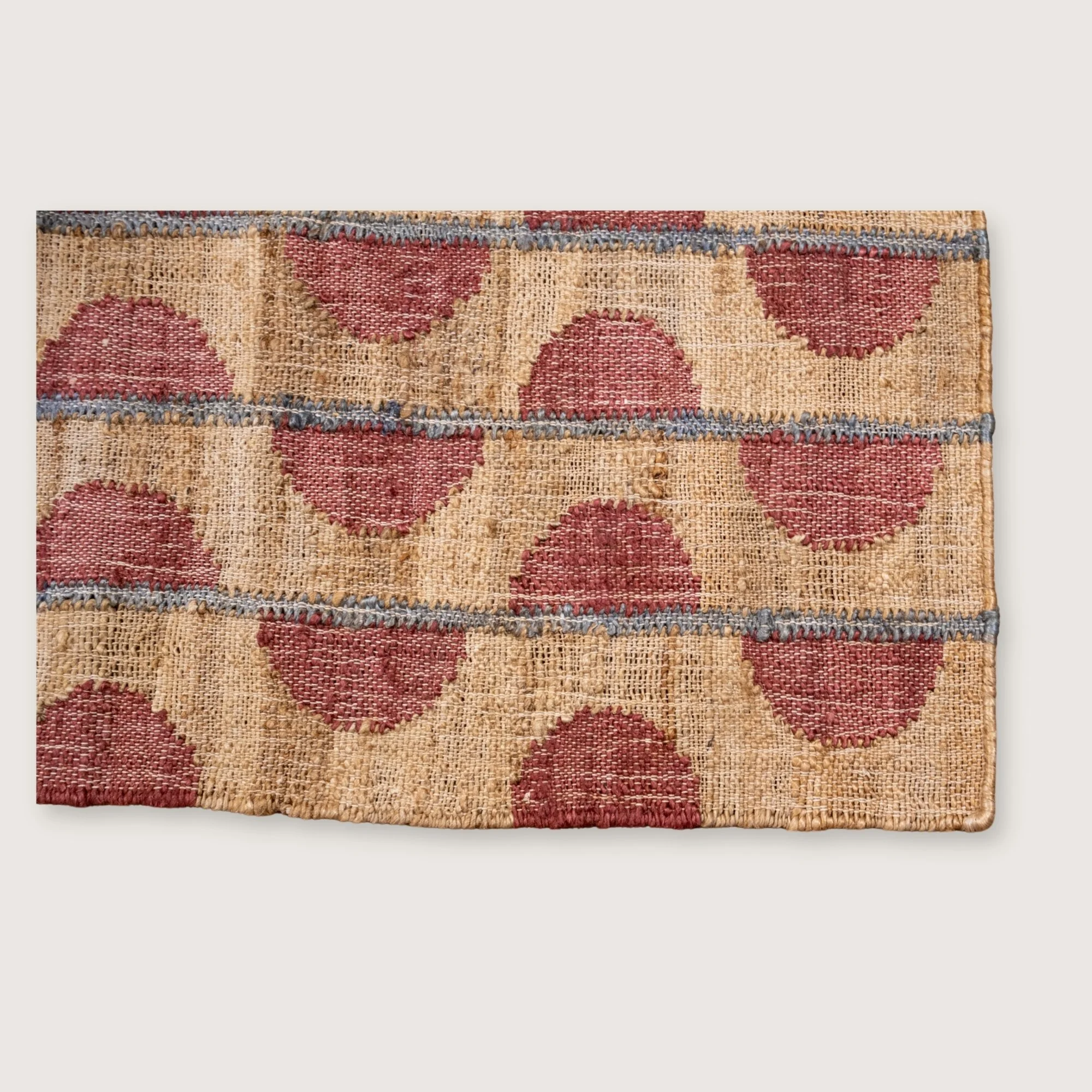 Handwoven jute rug with repeating half-moon pattern in dusty rose and natural sand tones.